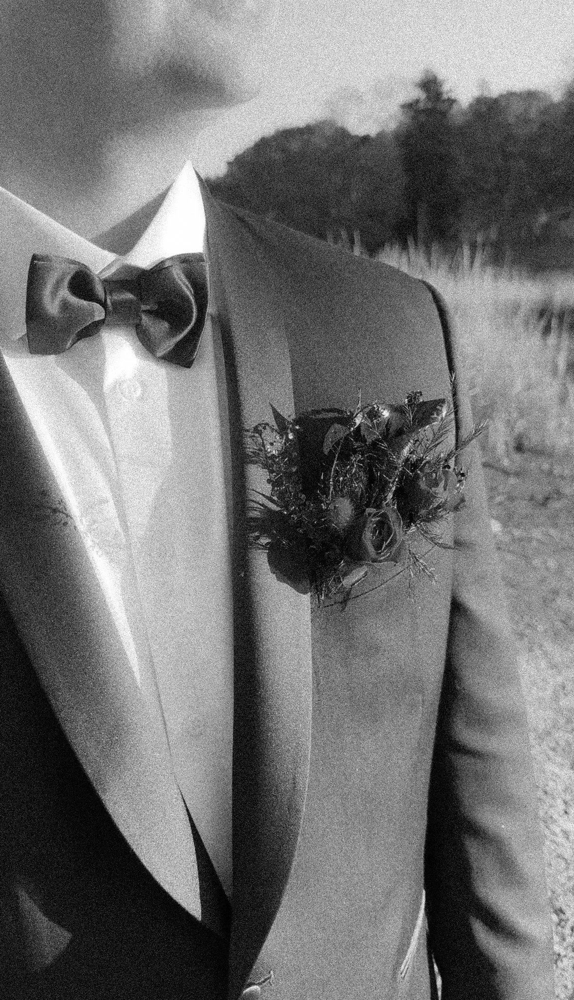 Close-up of a person wearing a suit jacket with a boutonniere and bow tie, taken outdoors in black and white by their wedding content creator