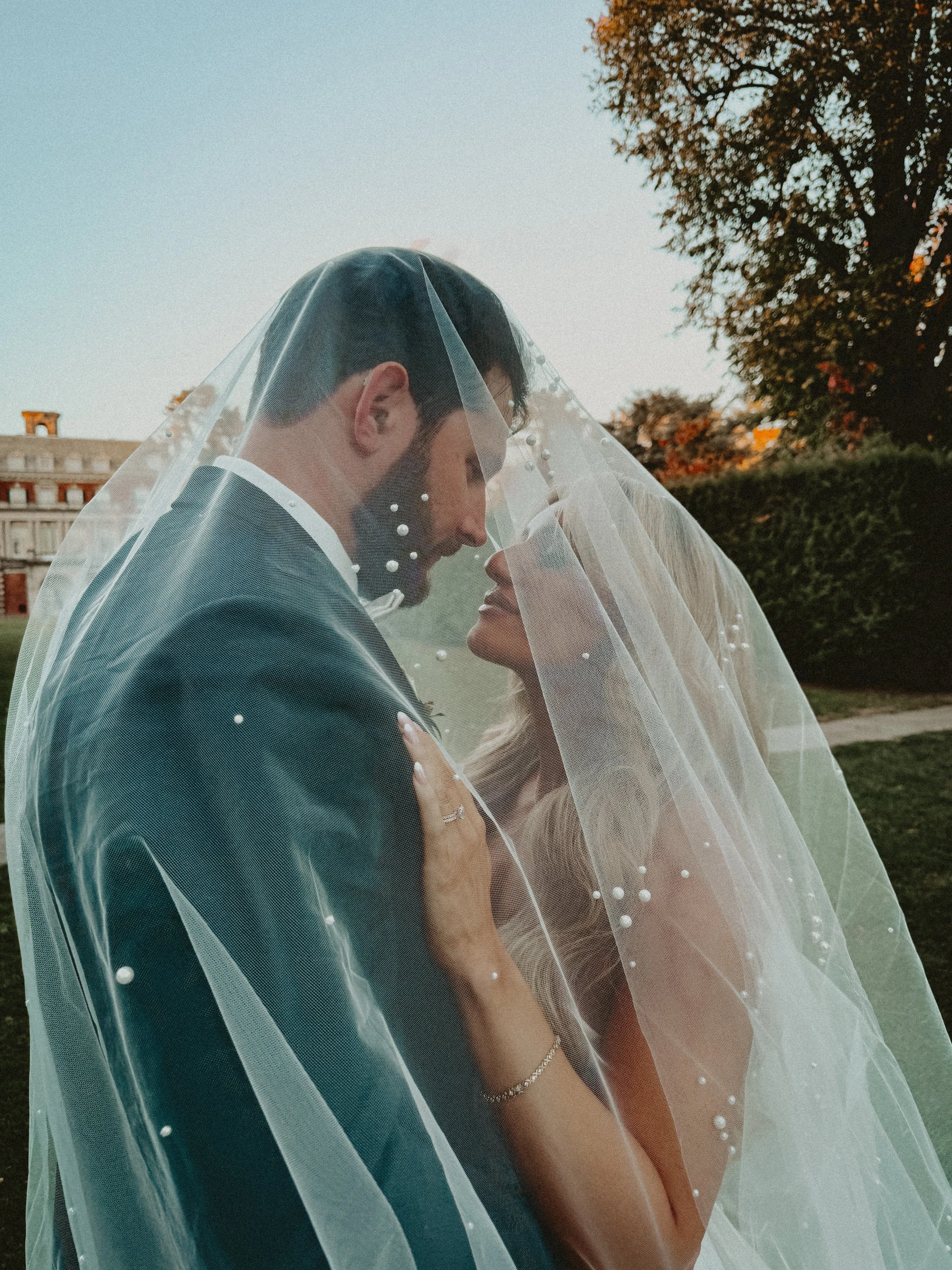 A bride and groom embrace under a wedding veil outdoors on their wedding day on Long Island, as their content creator captures the moment.