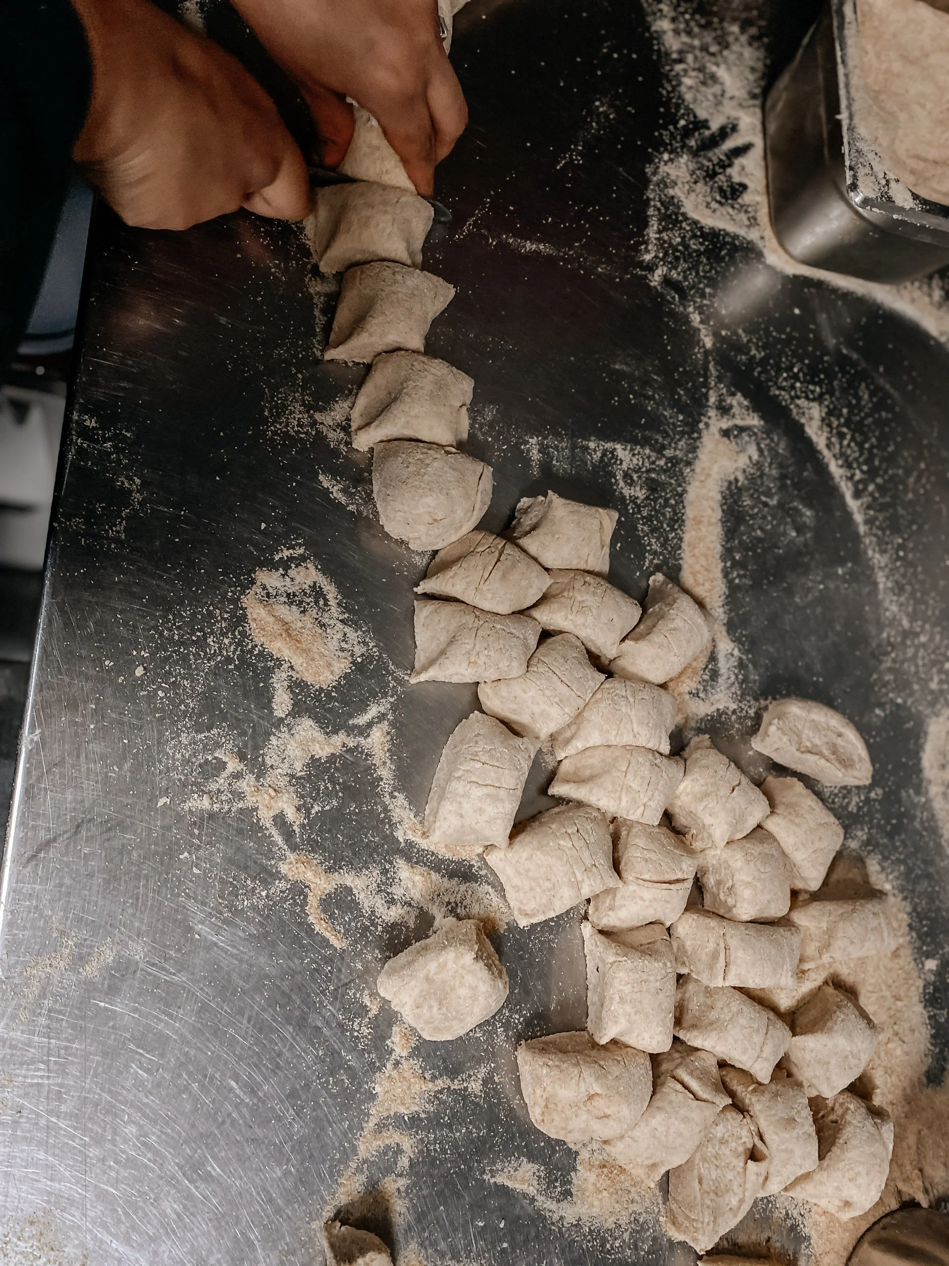 People rolling dough into small pieces on a floured metal surface.