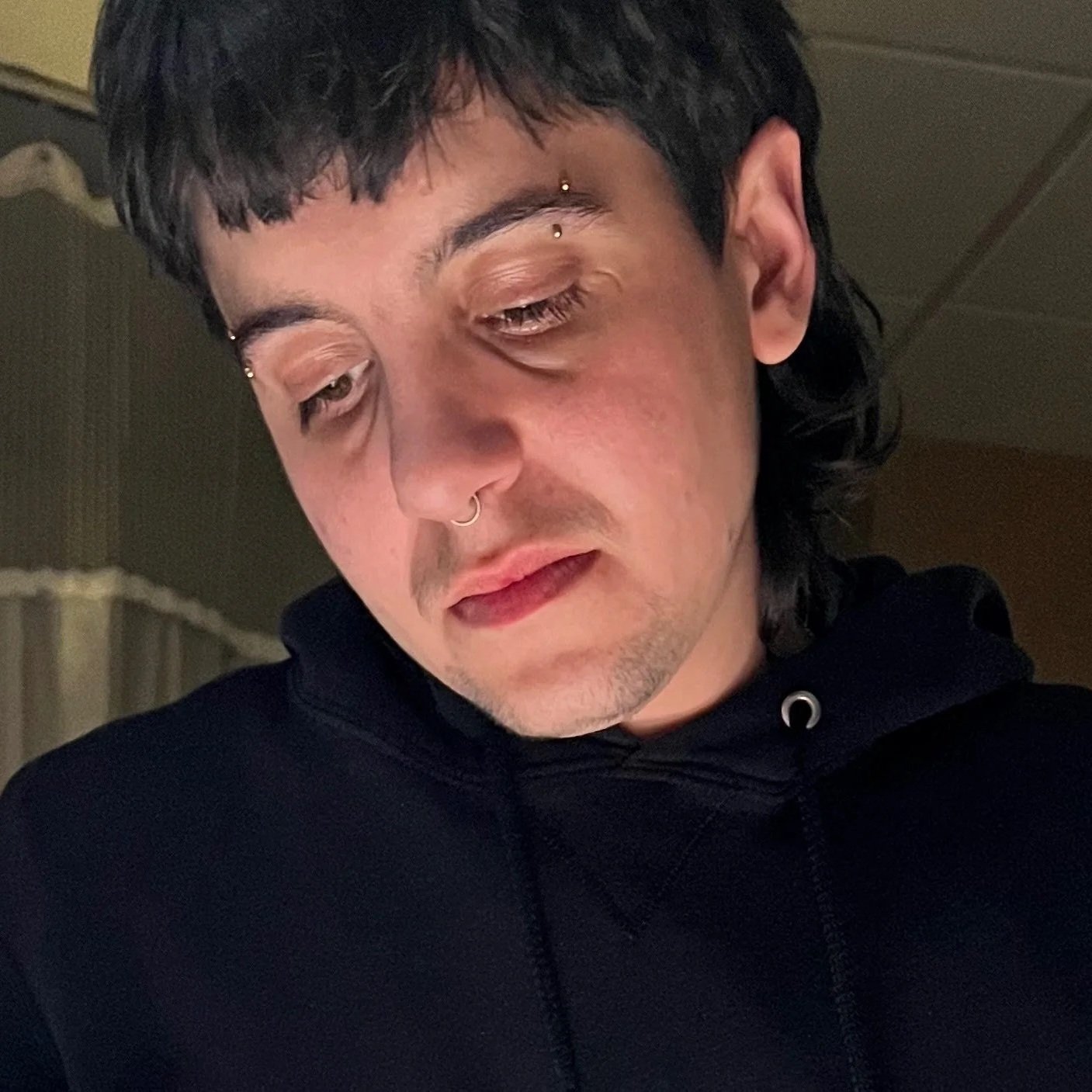 Joey is a white transmasculine person with dark hair, this is a close up of their head and shoulders as they watch a birth. A hospital curtain is visible behind them.