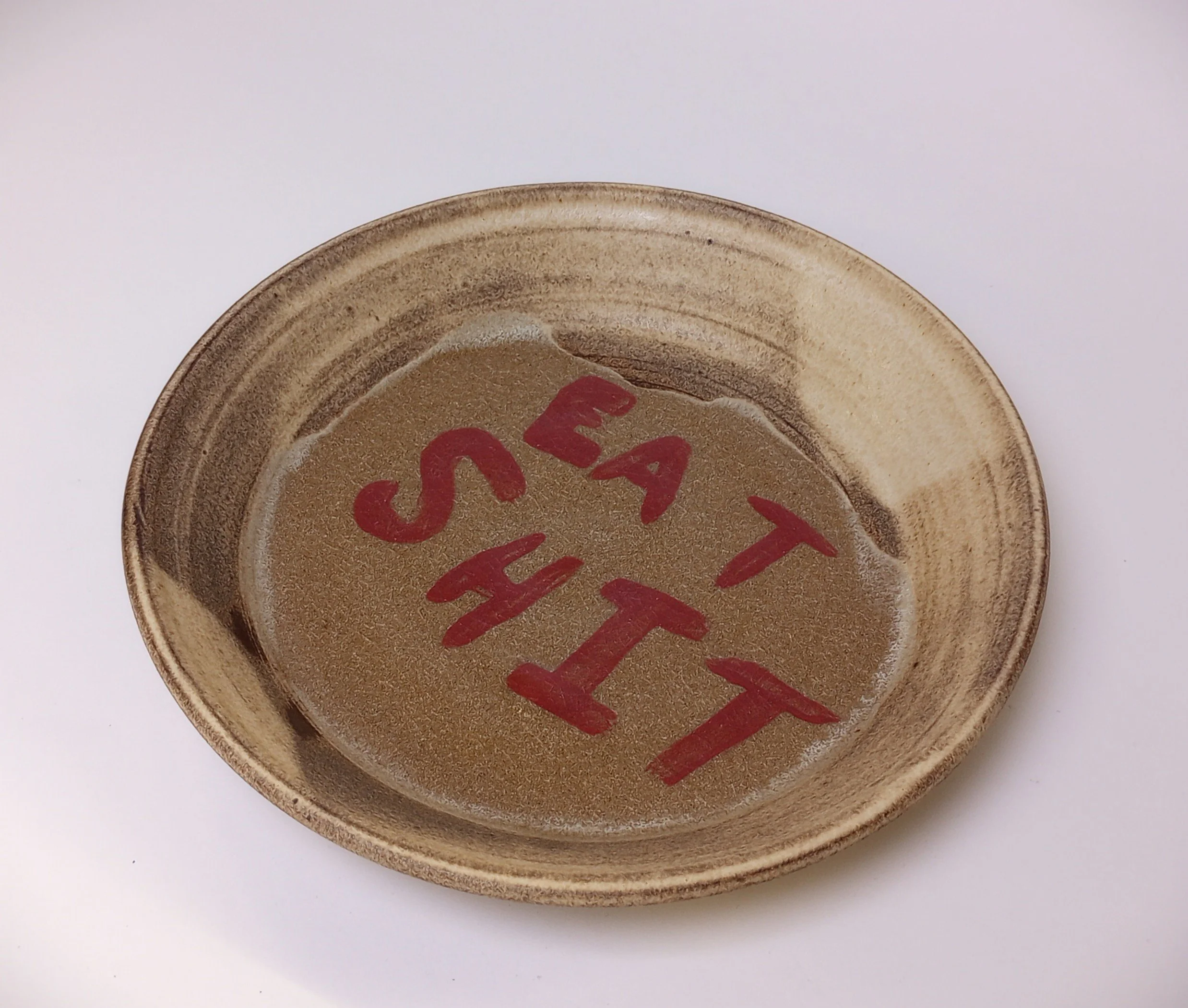 A ceramic plate that says "Eat Shit" in red letters. 