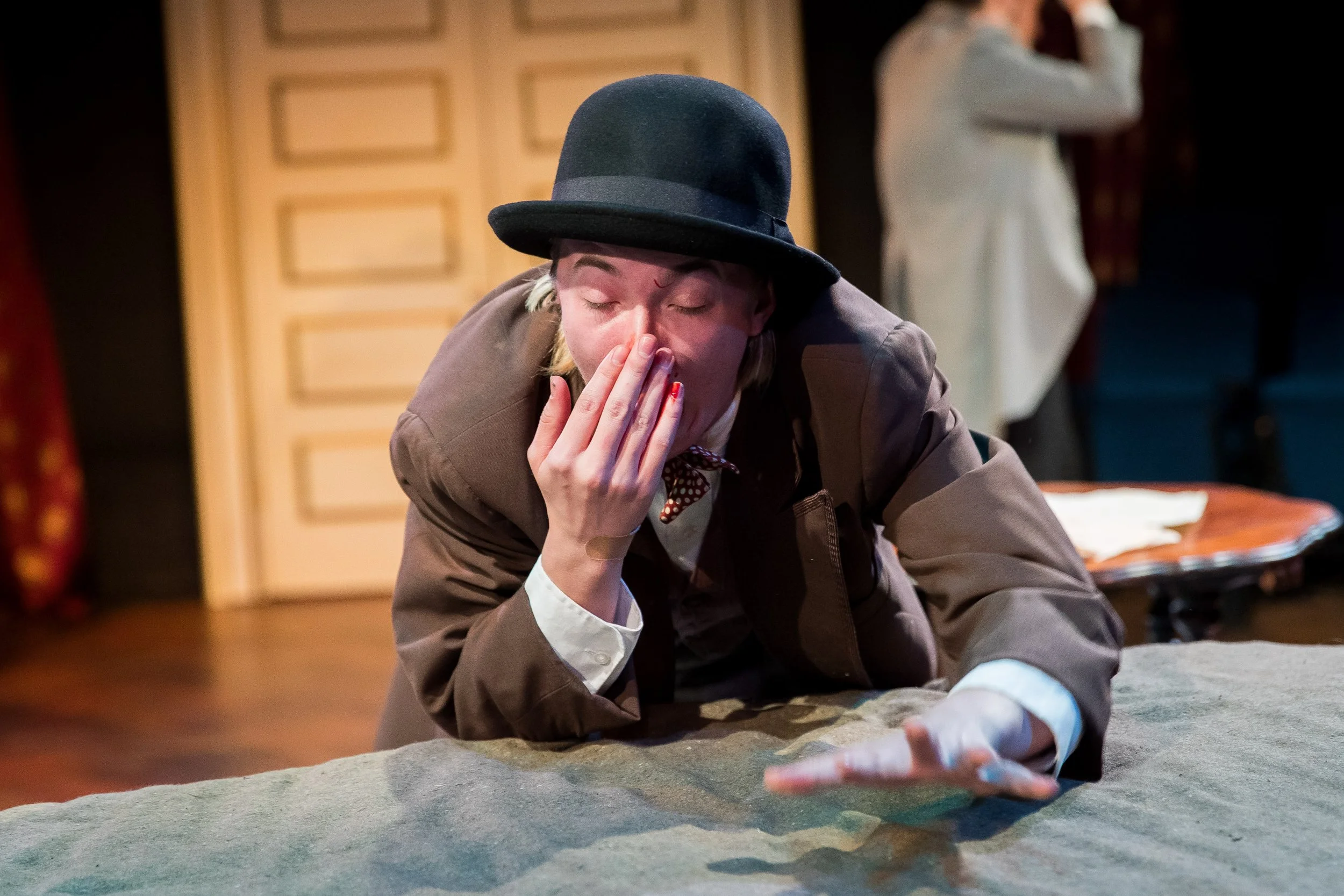 ZEWJ in a bowler hat leaning over a table with a fake bloody nose.