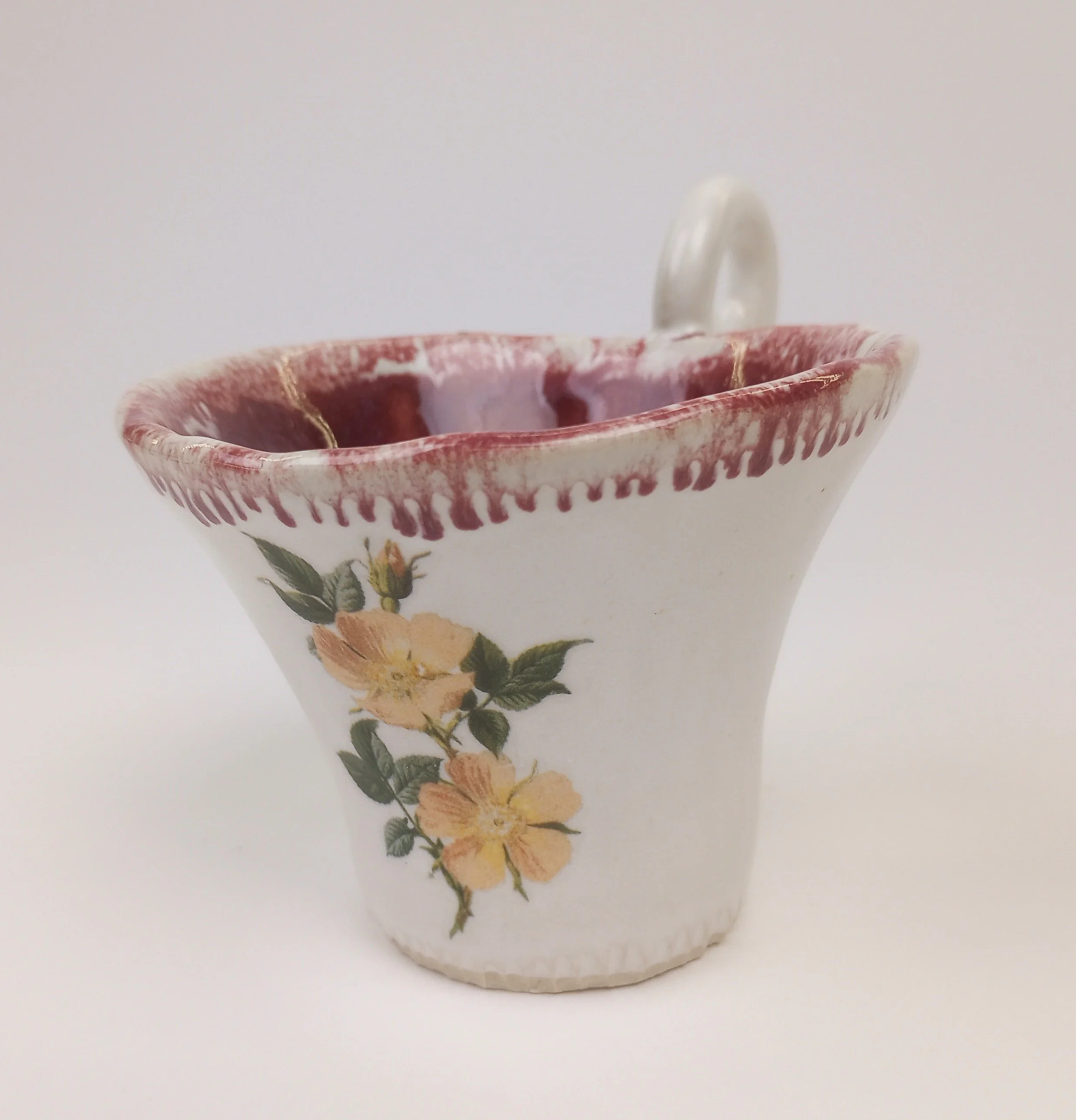 Close up of dainty white teacup with red rim and yellow flower decals.