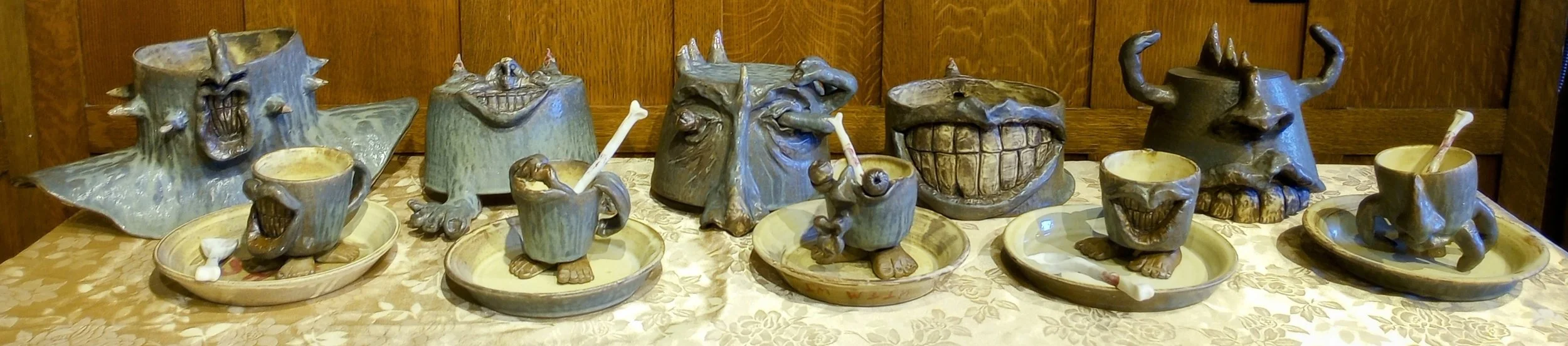 Row of gray ceramic helmets with faces, plates, and mugs with faces