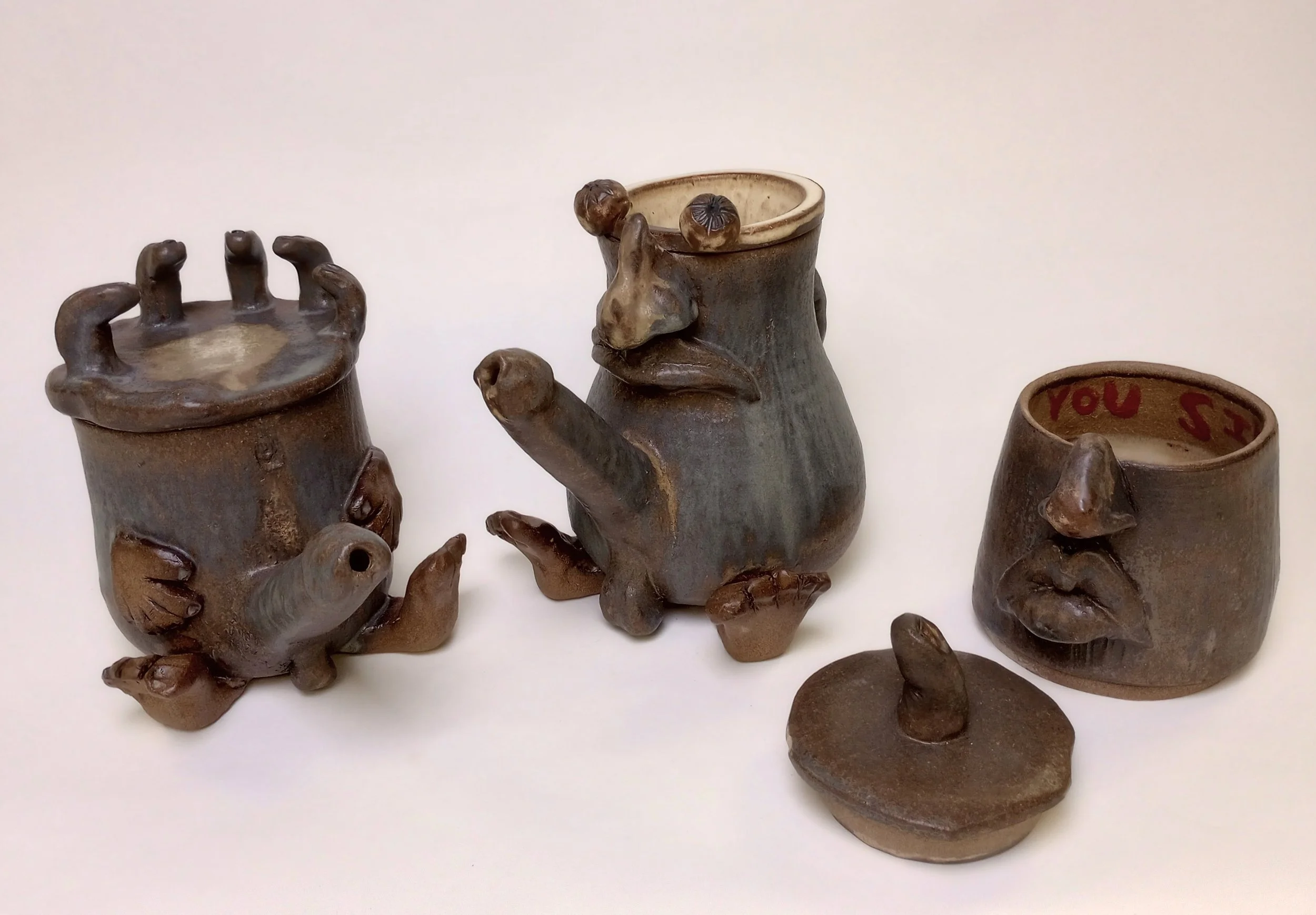 Two ceramic coffee pots with penis spouts beside a lid with finger handle and a coffee pot extension. 