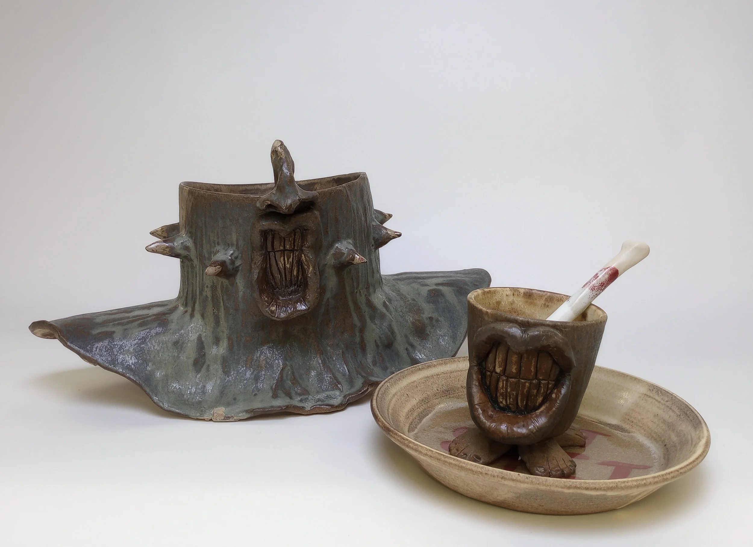 Smiling lower face and shoulder mask with spikes behind a smiling mug on plate.