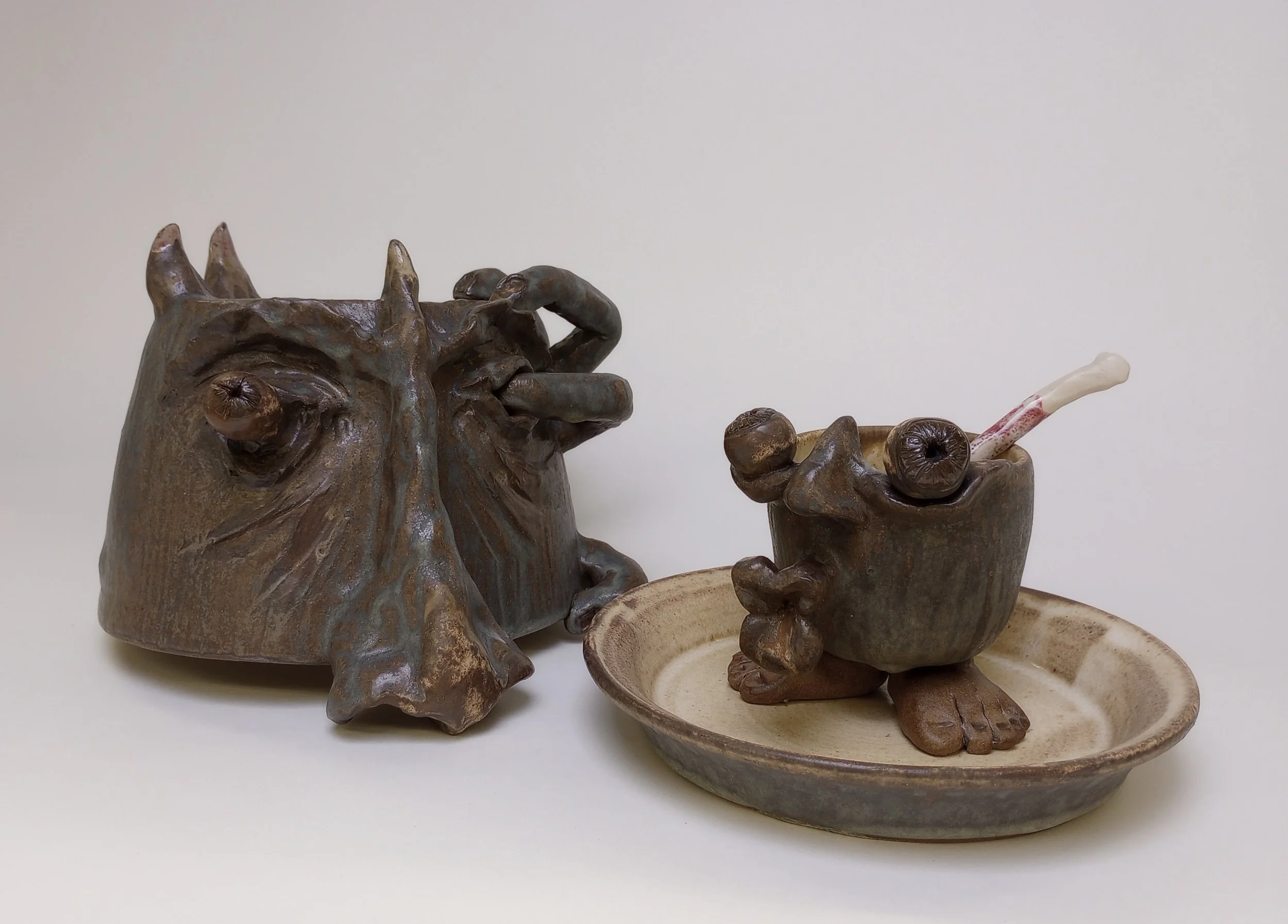 Helmet with large nose beside mug with lip handle on a plate.