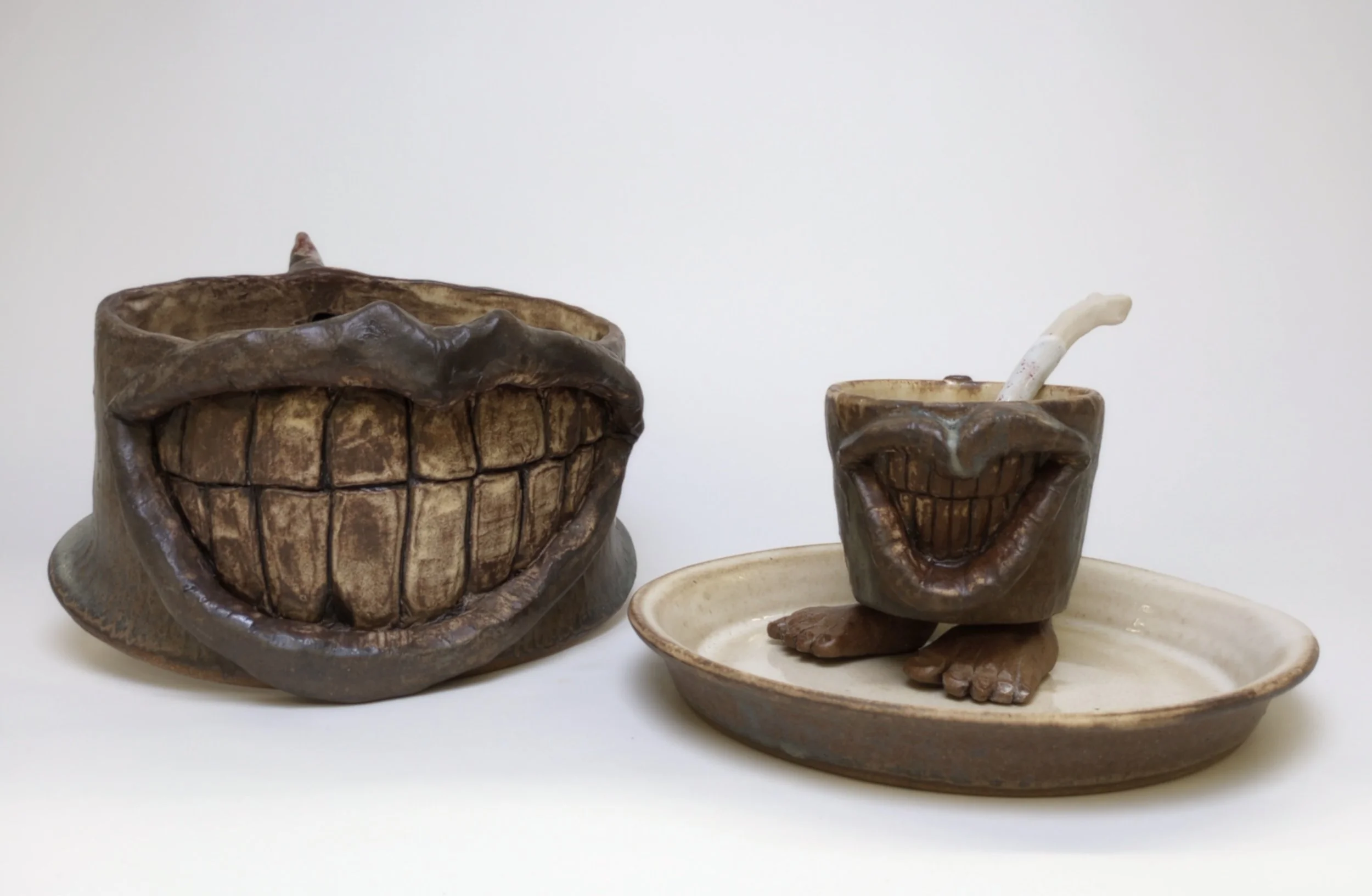 Mask with huge smiling mouth beside a mug with a mouth on a plate.