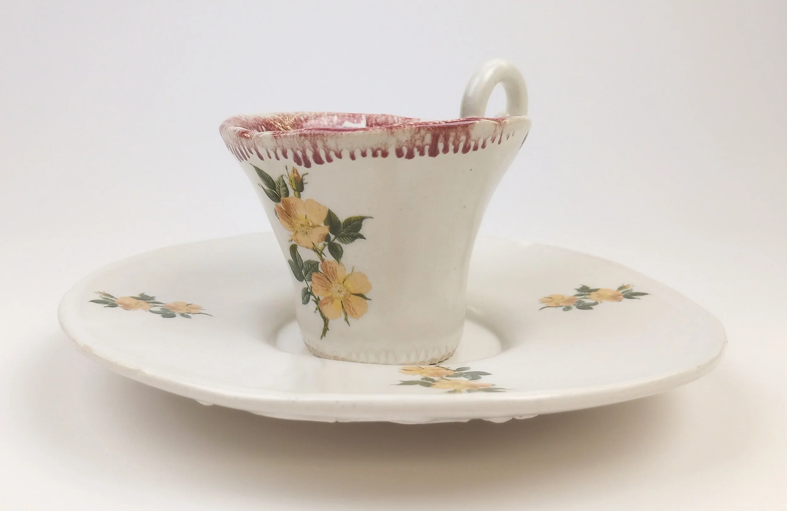White teacup with red rim and floral decals on a white plate with same floral decals.