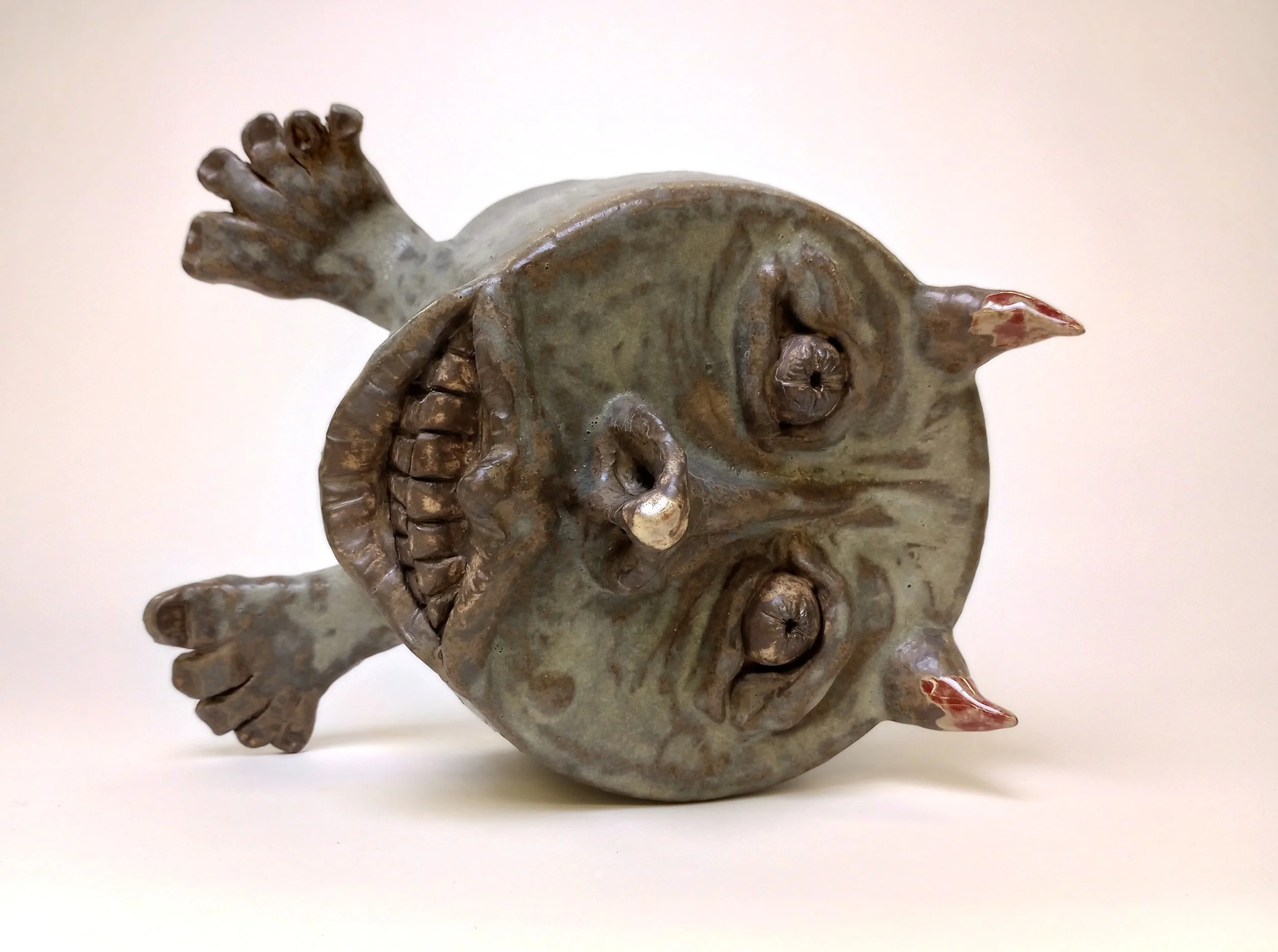 Top view of a ceramic helmet with feet, a face, and devil horns.