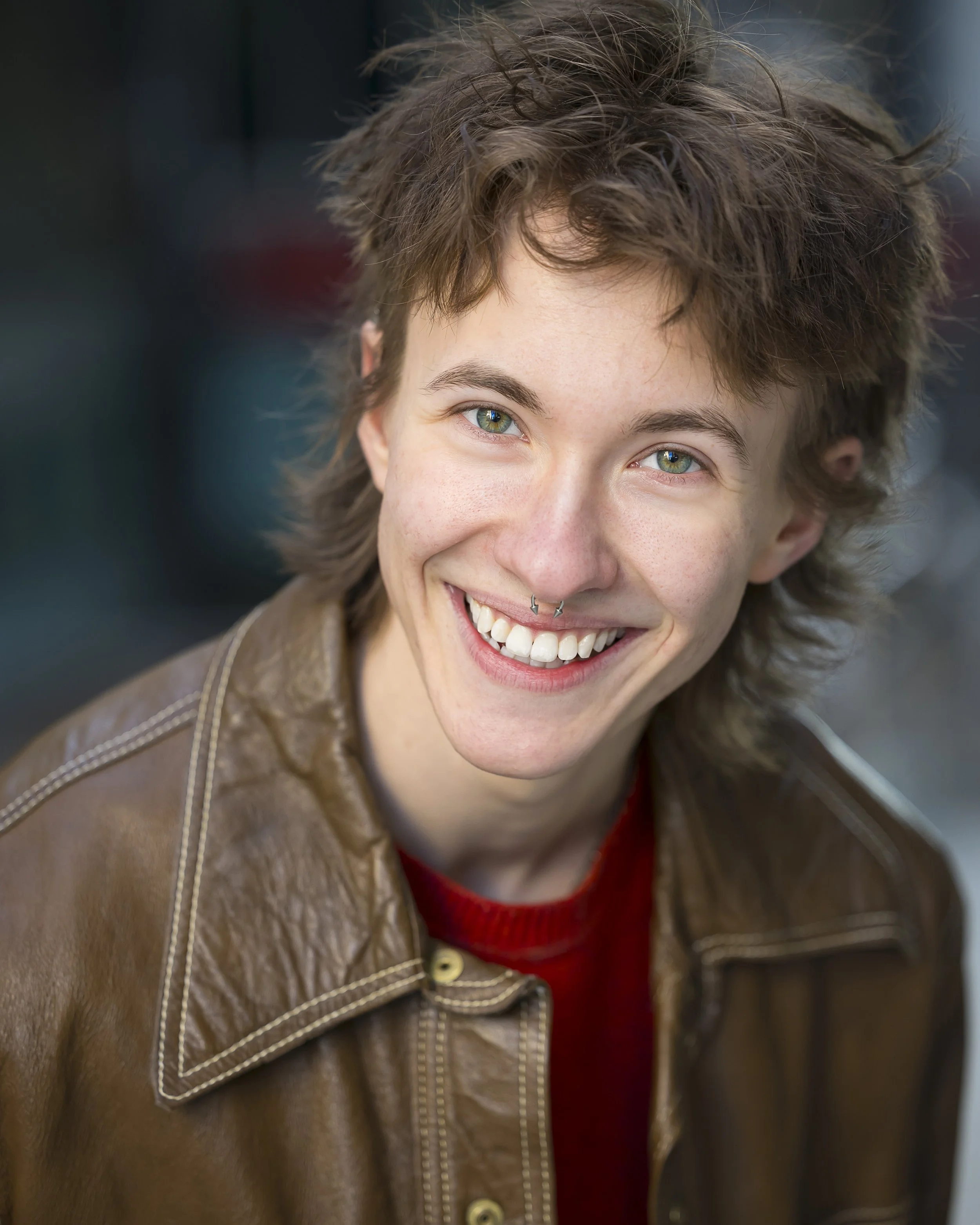 ZEWJ, a white trans guy in his 20s with brown hair and green eyes, smiling.
