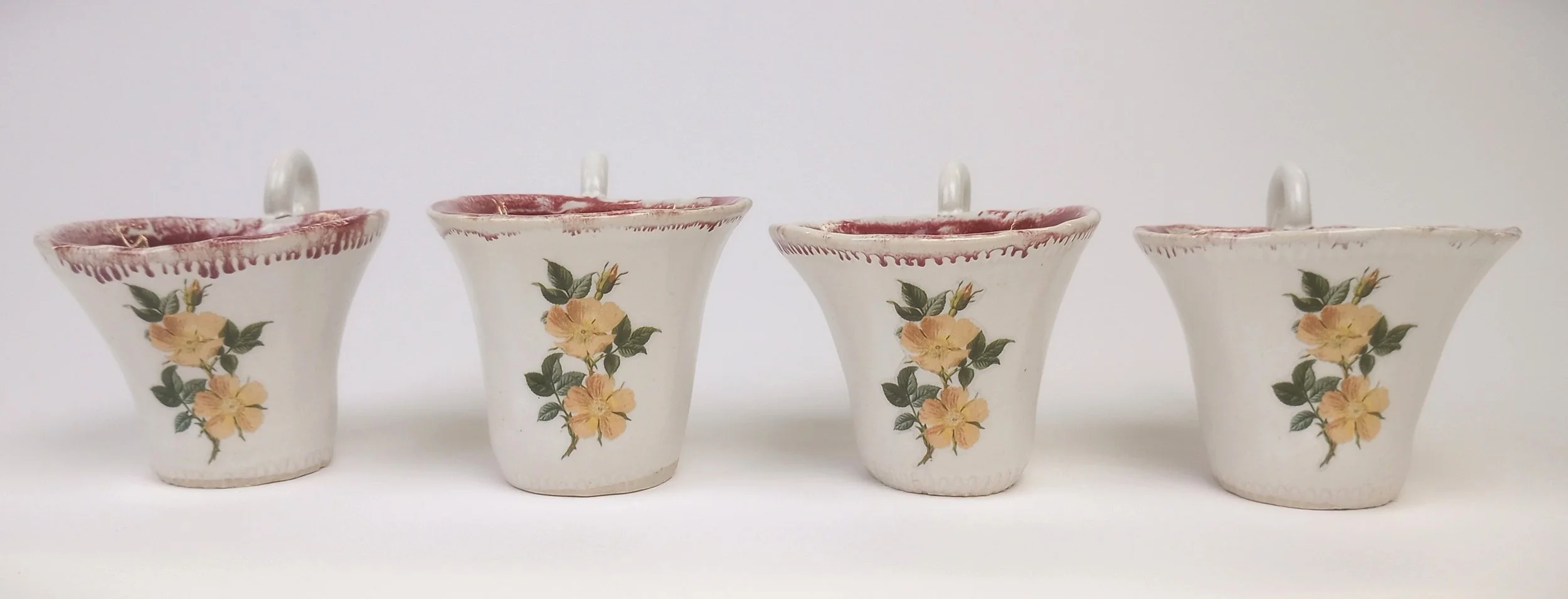 Line of four dainty white teacups with red rims and yellow floral decals.