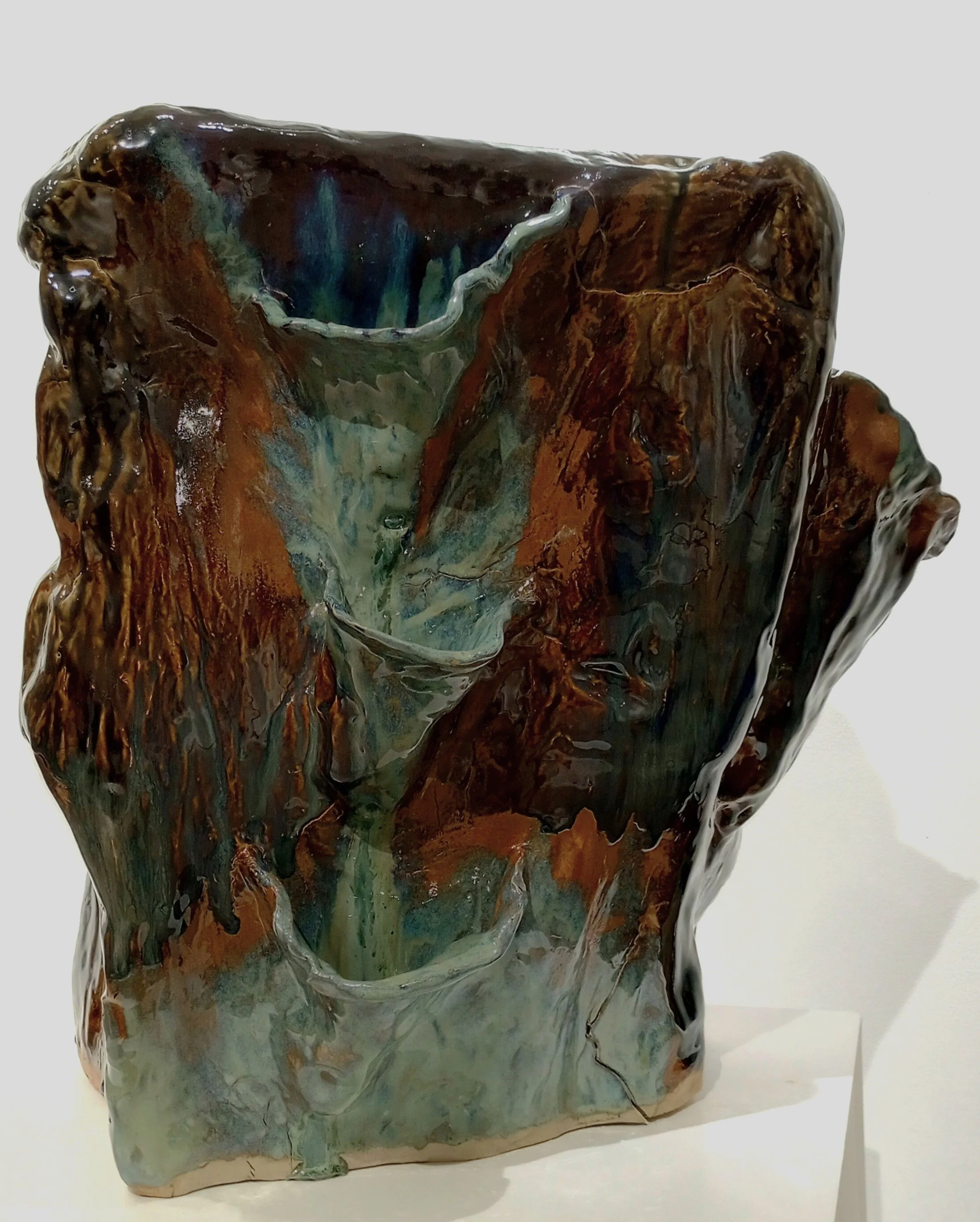Large brown, black, dark orange, gray, and blue ceramic sculpture with side pockets for plants.