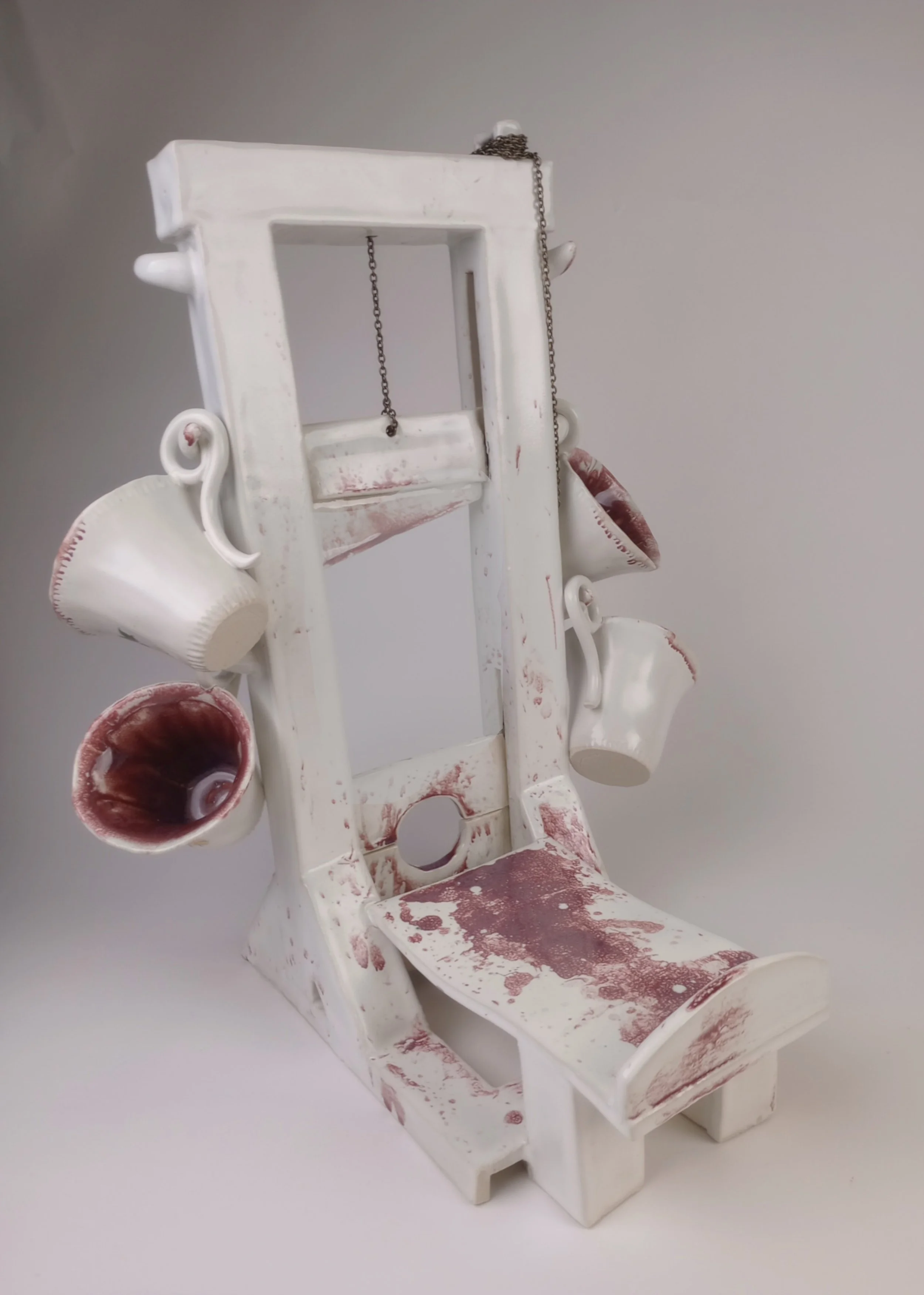Ceramic guillotine with four teacups hanging off hooks on sides.