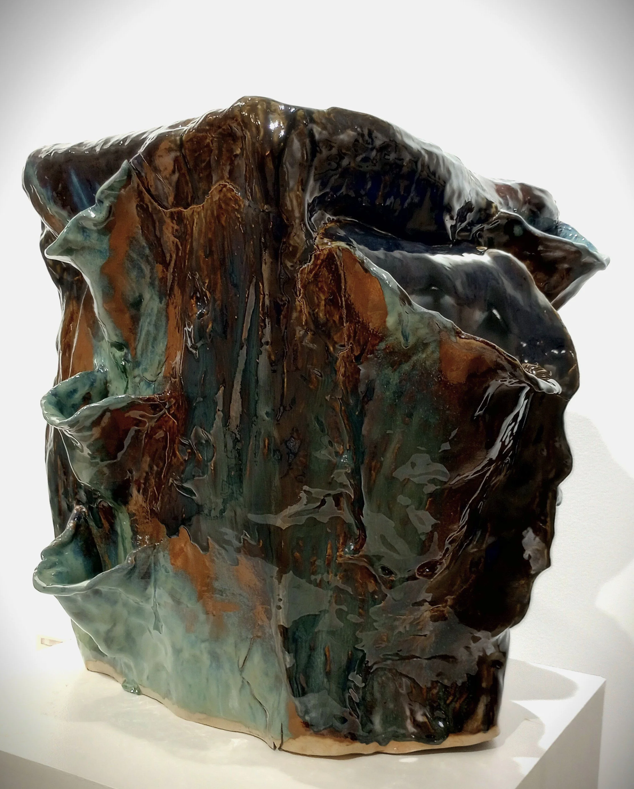 Large brown, black, dark orange, gray, and blue ceramic sculpture with three small side pockets and one large pocket for plants.
