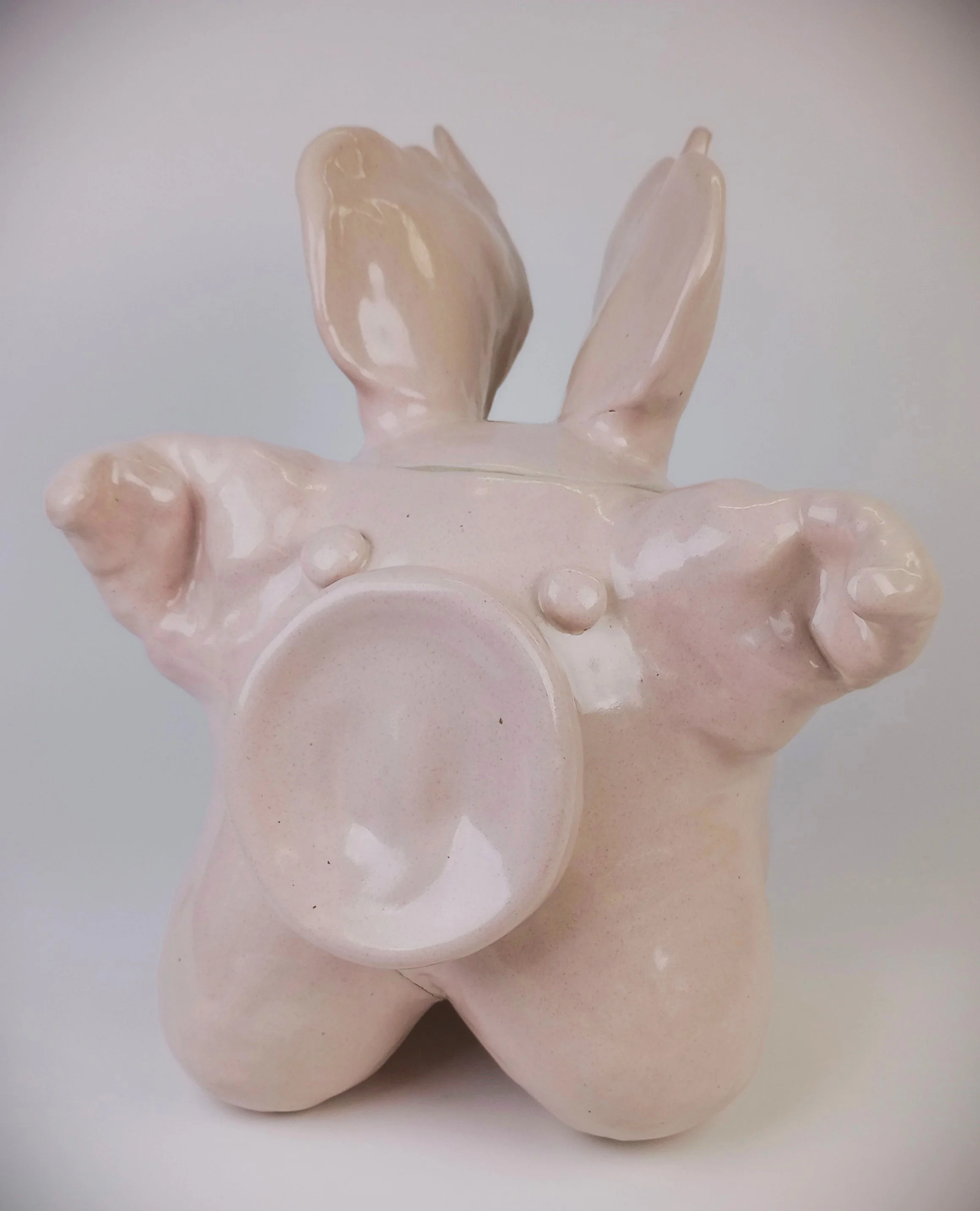Light pink pig sculpture with round legs, big nose, little eyes, wings, and big floppy ears.