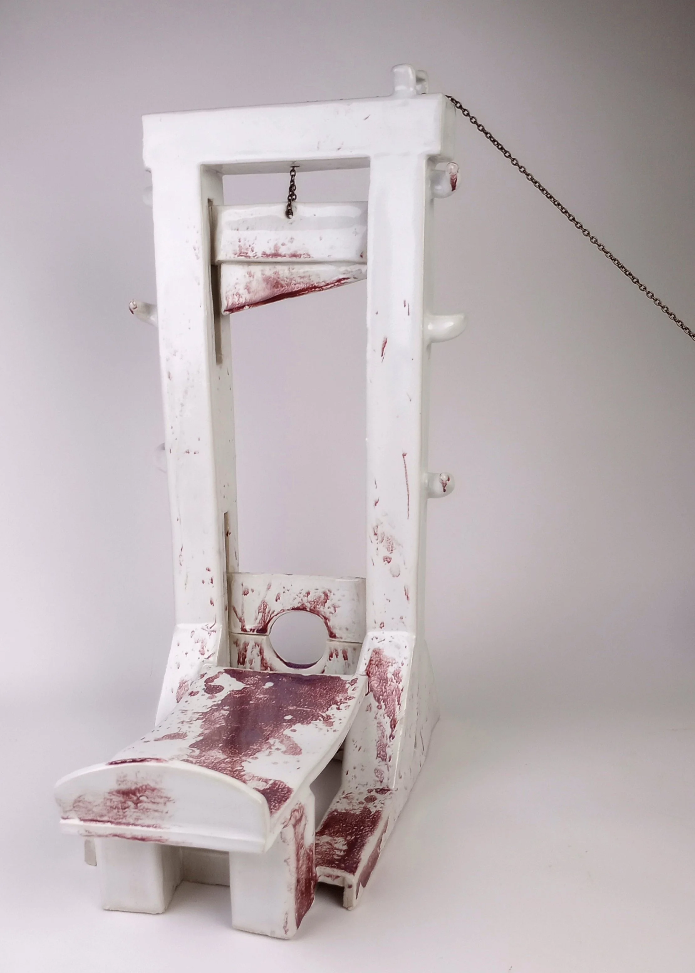 White ceramic guillotine with chain pulled taut and guillotine blade pulled up. 