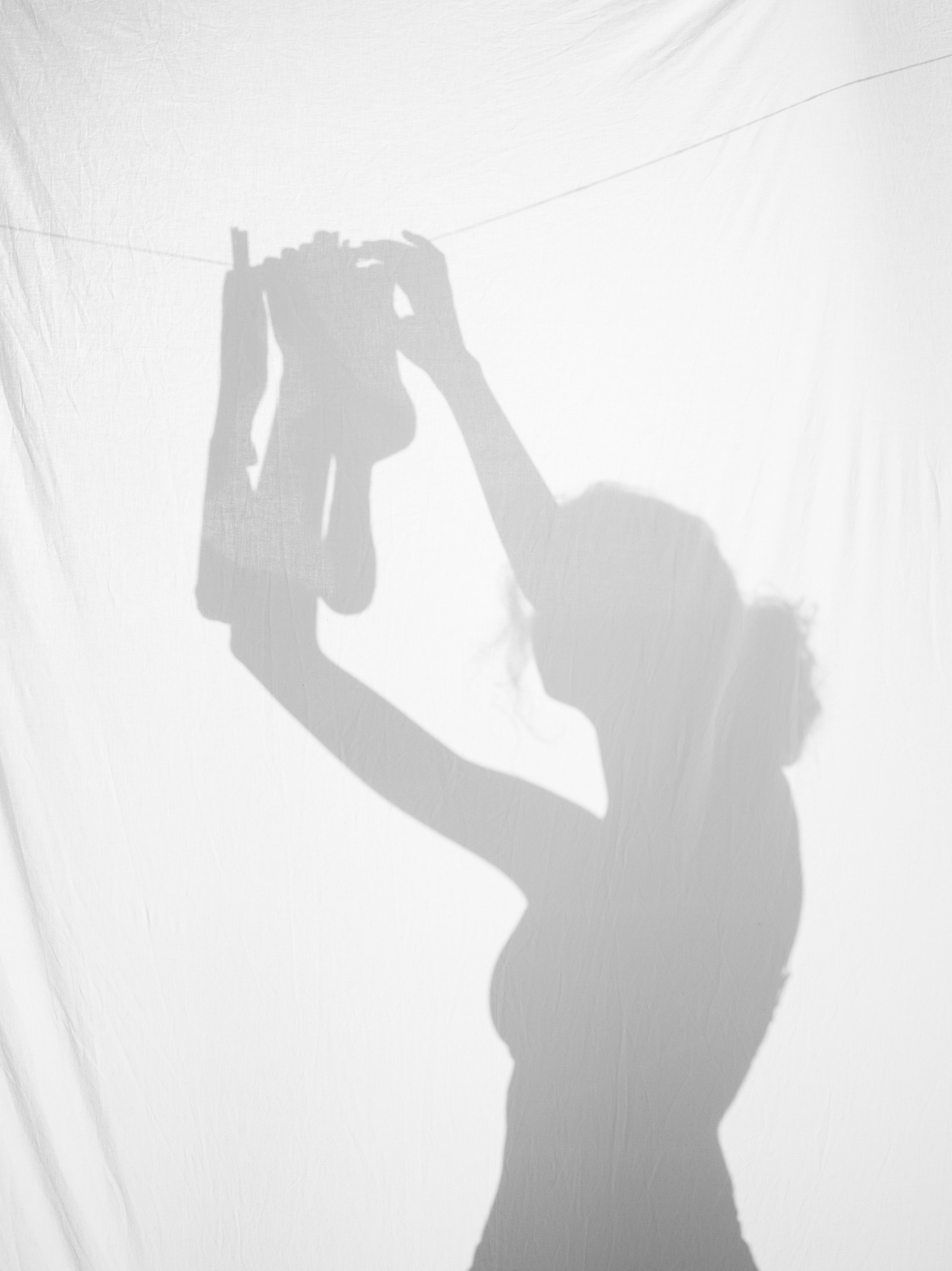 Silhouette of a woman holding a camera, casting a shadow on a white background.