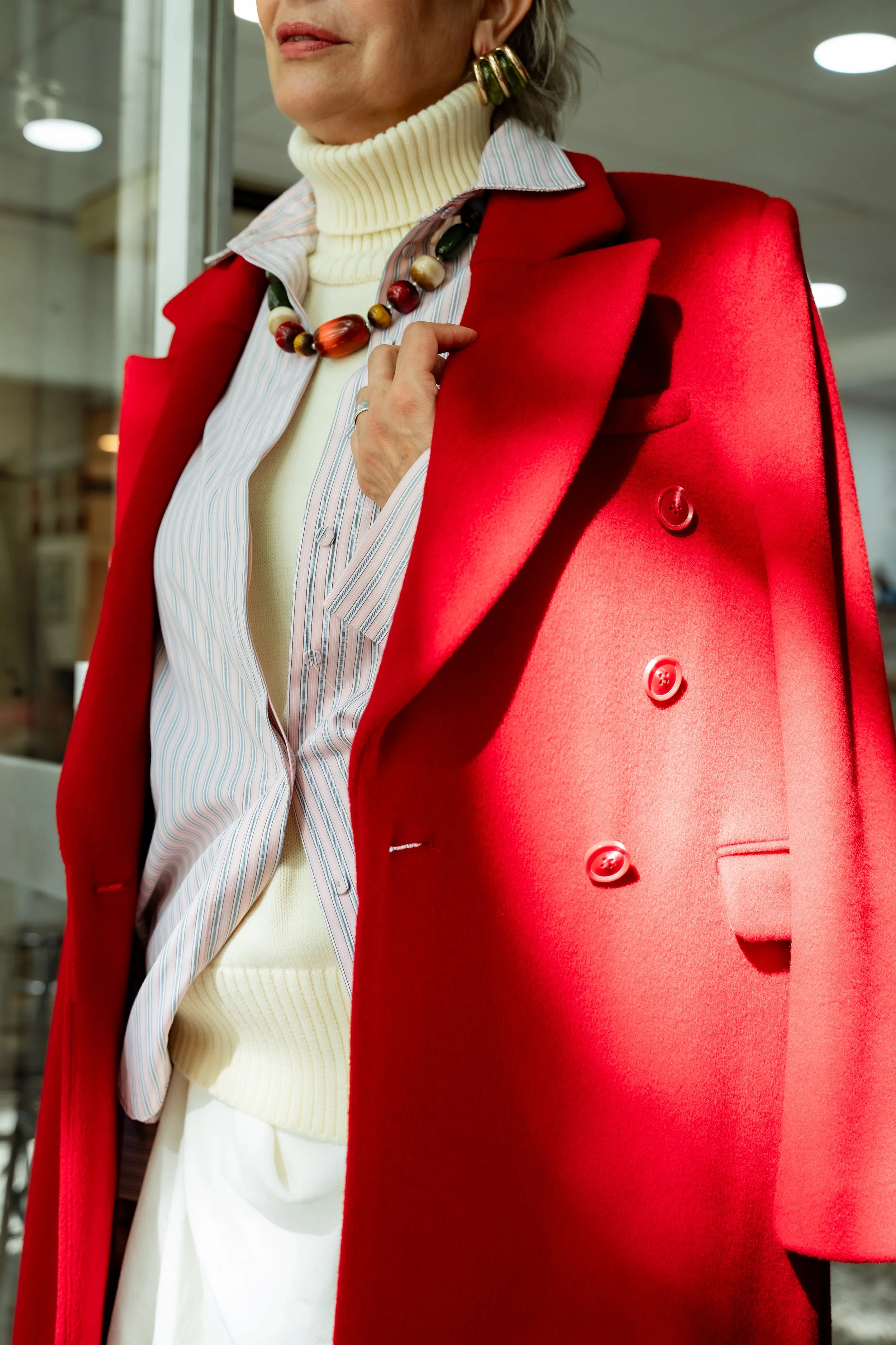 Close-up of a woman wearing a red coat, a turtleneck sweater, layered with a striped shirt, and a colorful beaded necklace.
