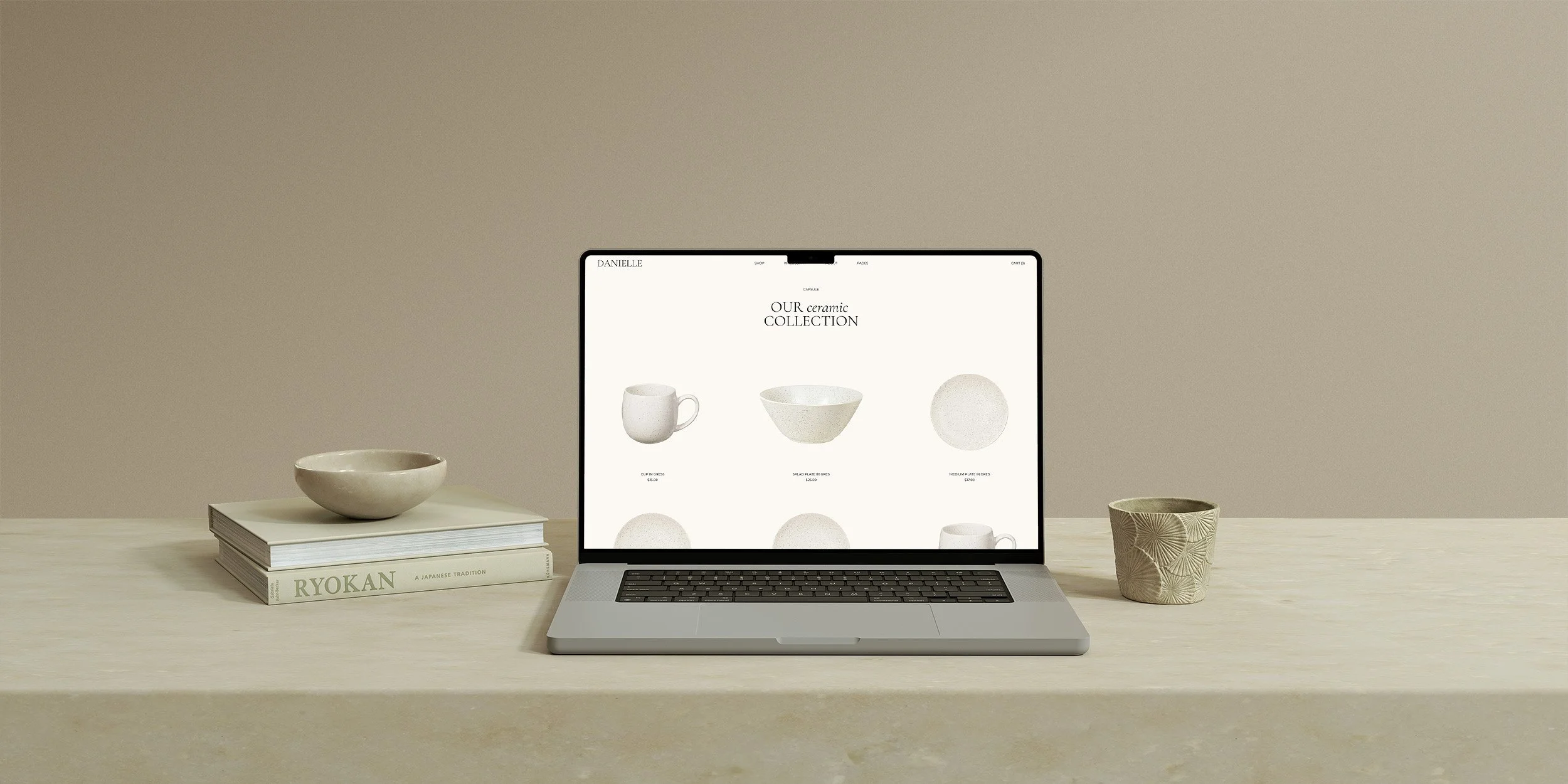 Verso Visual - Squarespace E-commerce Template - Laptop displaying a ceramics online store, flanked by a bowl on a stack of books on the left and a patterned cup on the right, on a light-colored wooden surface against a plain beige background.
