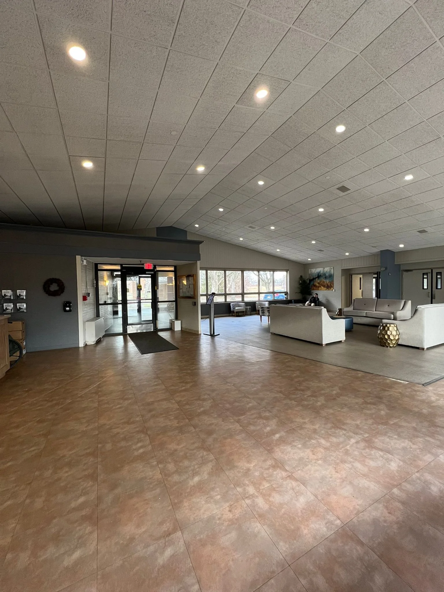 A spacious lobby with tiled floor, seating area with sofas and chairs, large window letting in natural light, and a decorative gold side table.