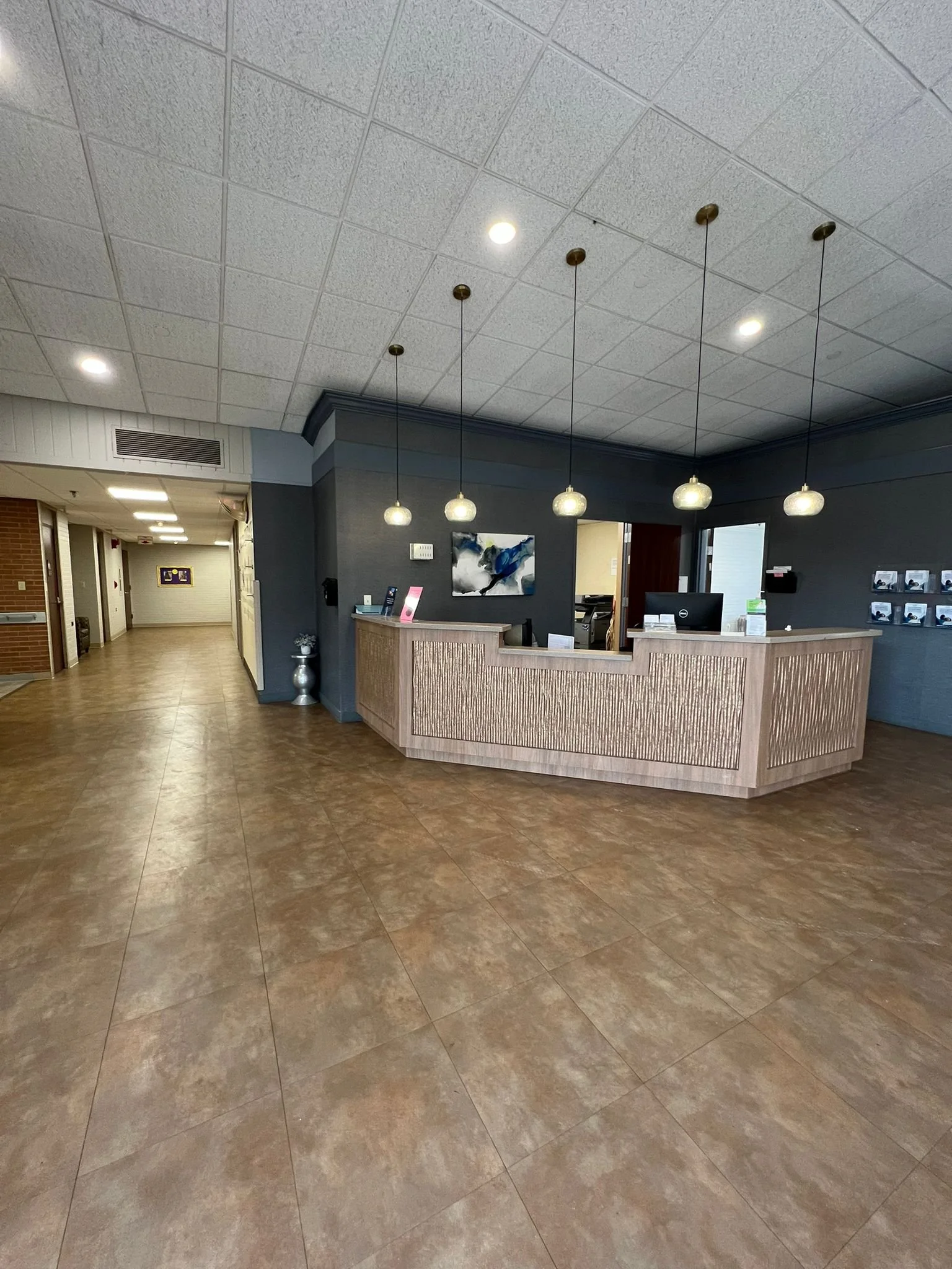 Empty lobby with a wooden reception desk, hanging pendant lights, and a hallway to the left.