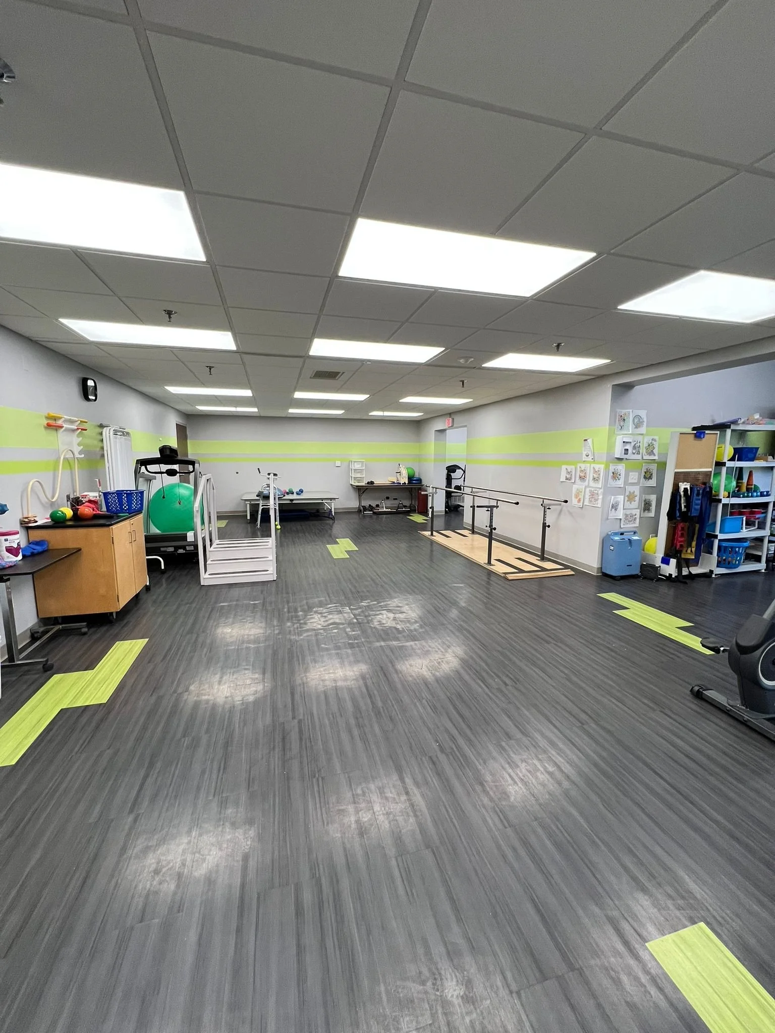 Empty therapy or rehabilitation room with exercise equipment, handrails, and colorful floor markings.