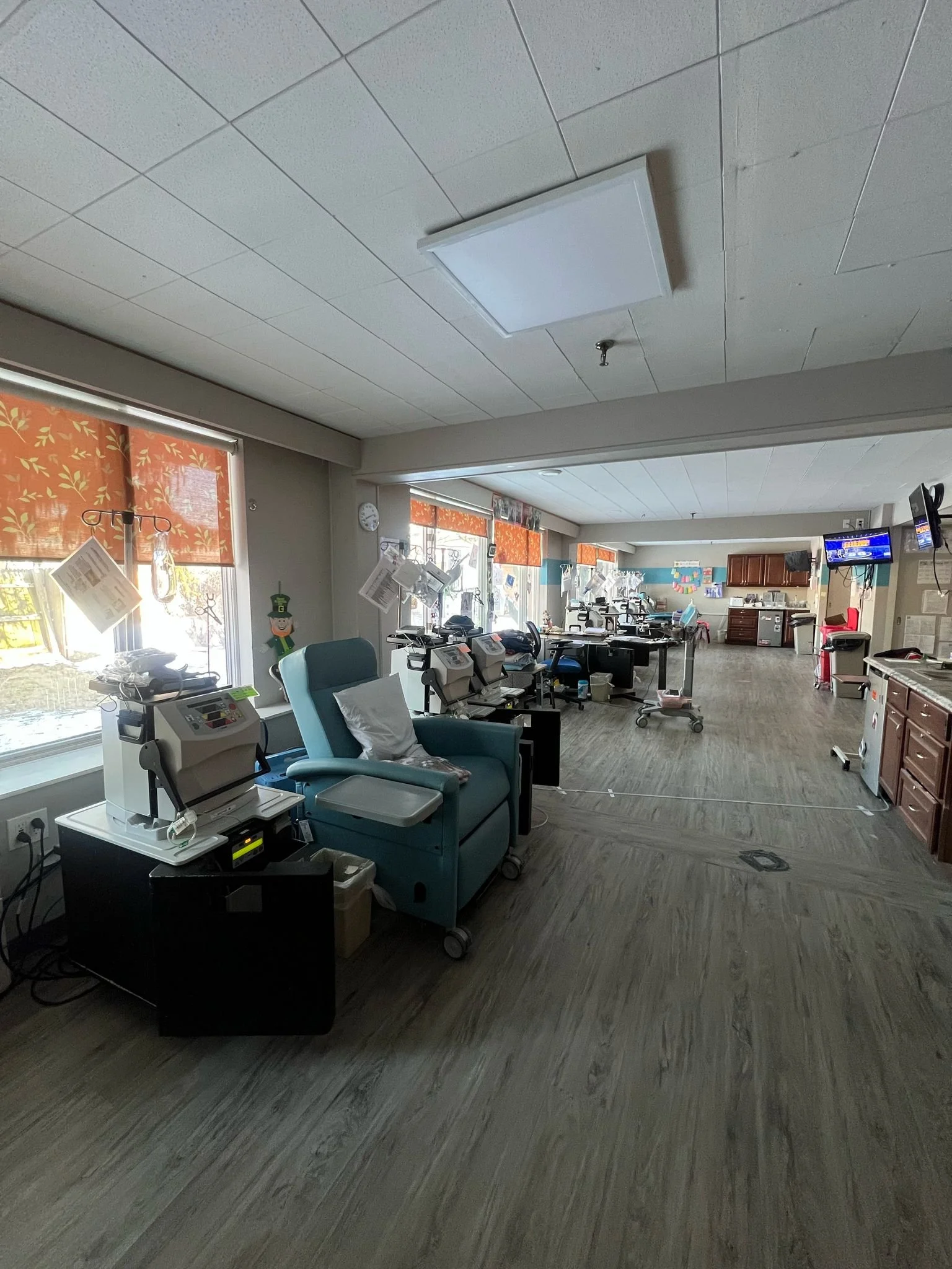 A medical room with multiple chairs, medical equipment, and monitors, decorated with holiday-themed curtains and decorations, likely a dialysis or treatment center.