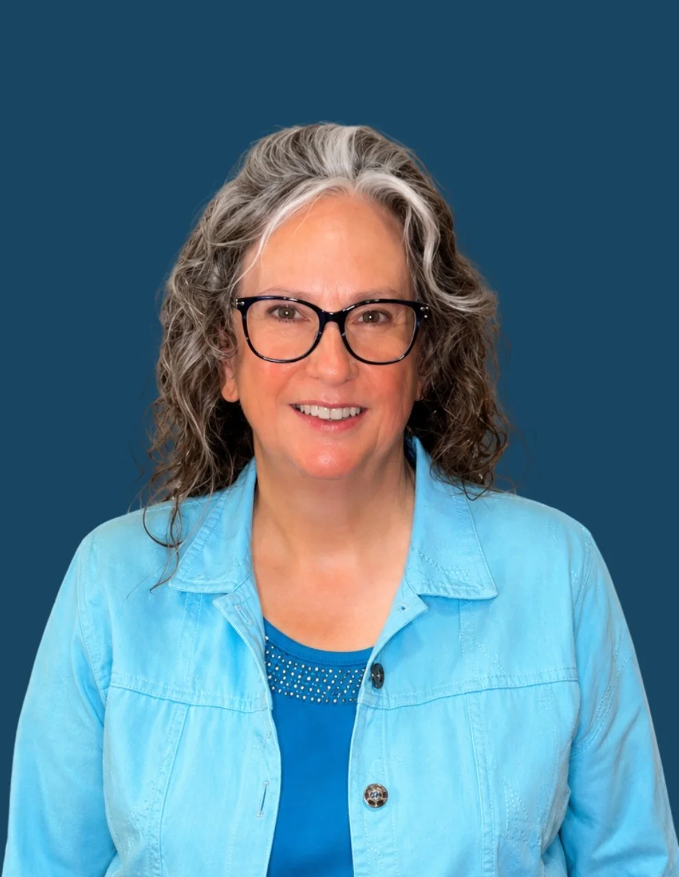 Portrait of Johnna Shaferly, Social Services Coordinator, smiling while wearing black-framed glasses, a light blue jacket, and a blue top against a dark blue circular background.