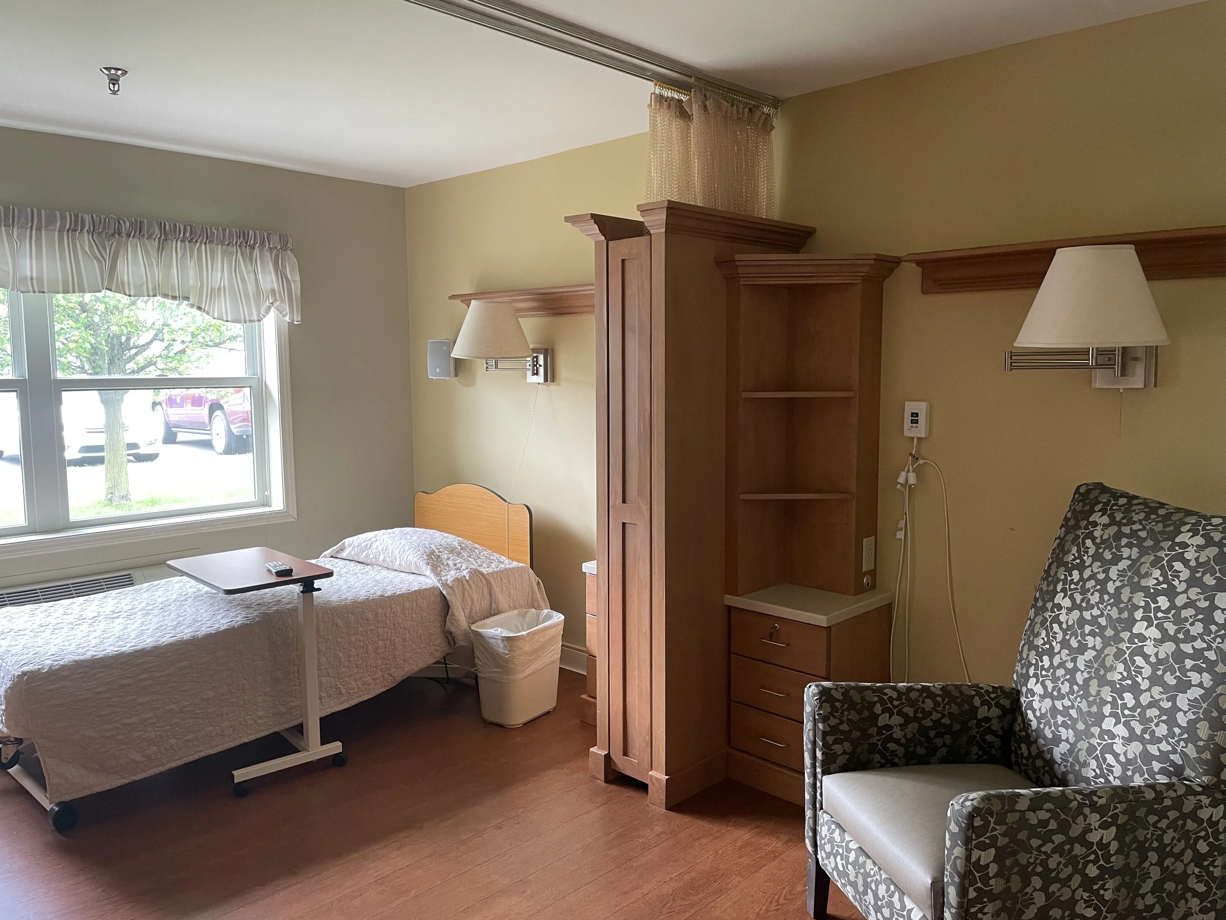 Bright and comfortable private skilled nursing room at Fieldstone Nursing and Rehabilitation Center with a hospital bed, seating area, and large window view.