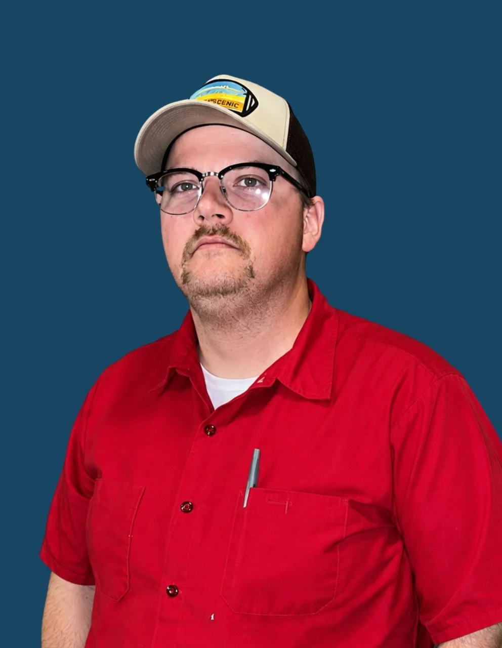 Portrait of Evan Fry, Plant Operations Supervisor, wearing a red button-up work shirt, glasses, and a tan baseball cap, posed against a dark blue circular background.