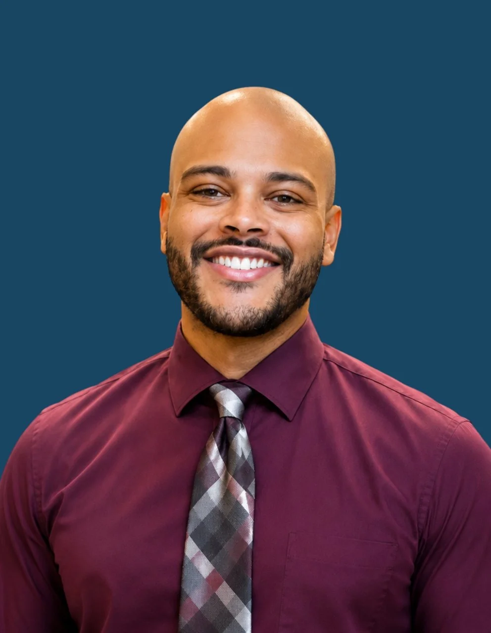 Portrait of Tyler Mason, RN, BSN, LNHA, Administrator, smiling at the camera while wearing a burgundy dress shirt and patterned tie against a dark blue circular background.