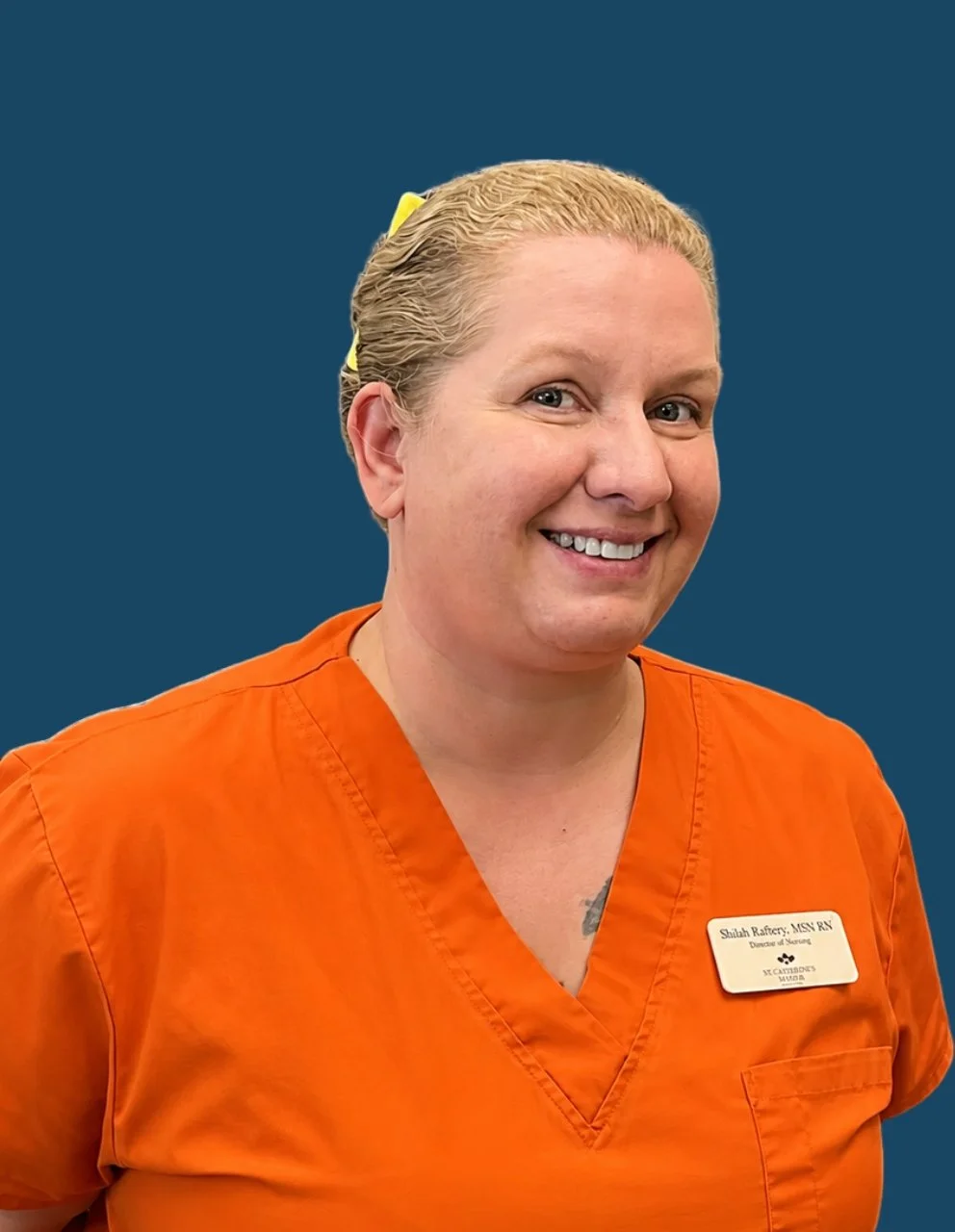 Portrait of Shiloh Rafferty, RN, MSN, Director of Nursing, smiling and wearing bright orange nursing scrubs against a dark blue circular background.