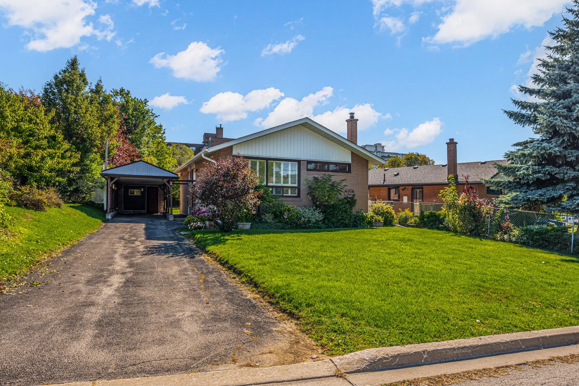 Front view of a suburban house with a driveway, surrounded by a well-maintained lawn and garden, under a blue sky with scattered clouds.