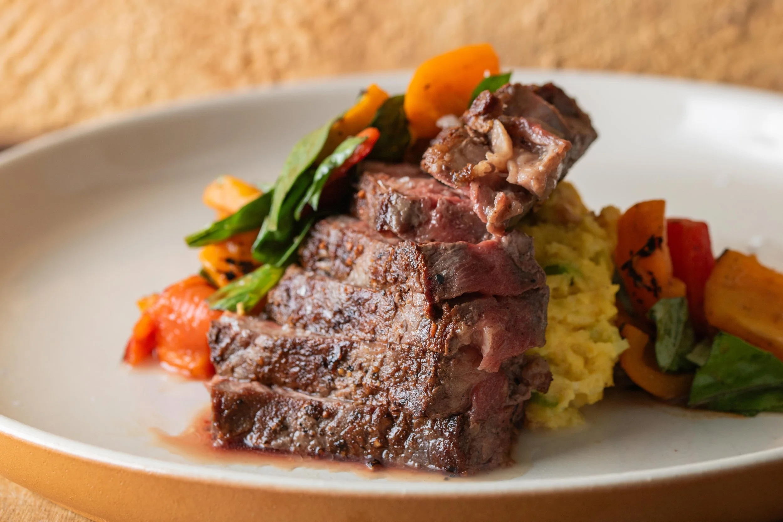 A plated dish featuring a serving of cooked beef short ribs with a side of mashed potatoes and roasted vegetables, including carrots and zucchini.