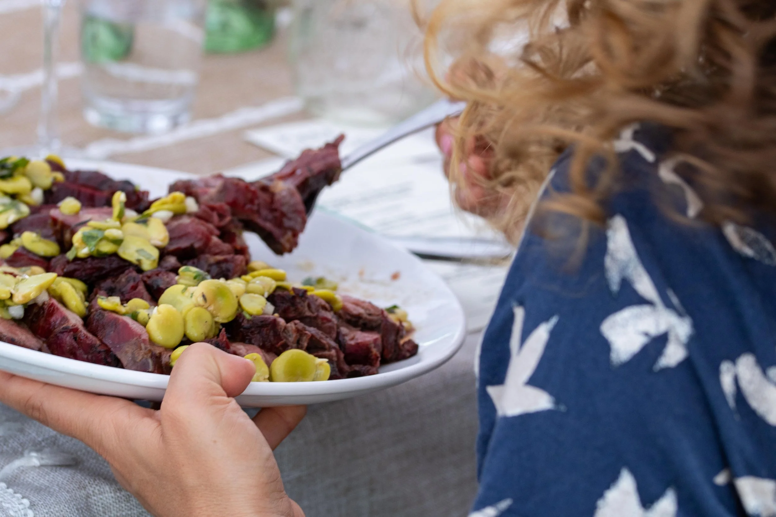 Person holding a white plate of cooked beef topped with green grapes.