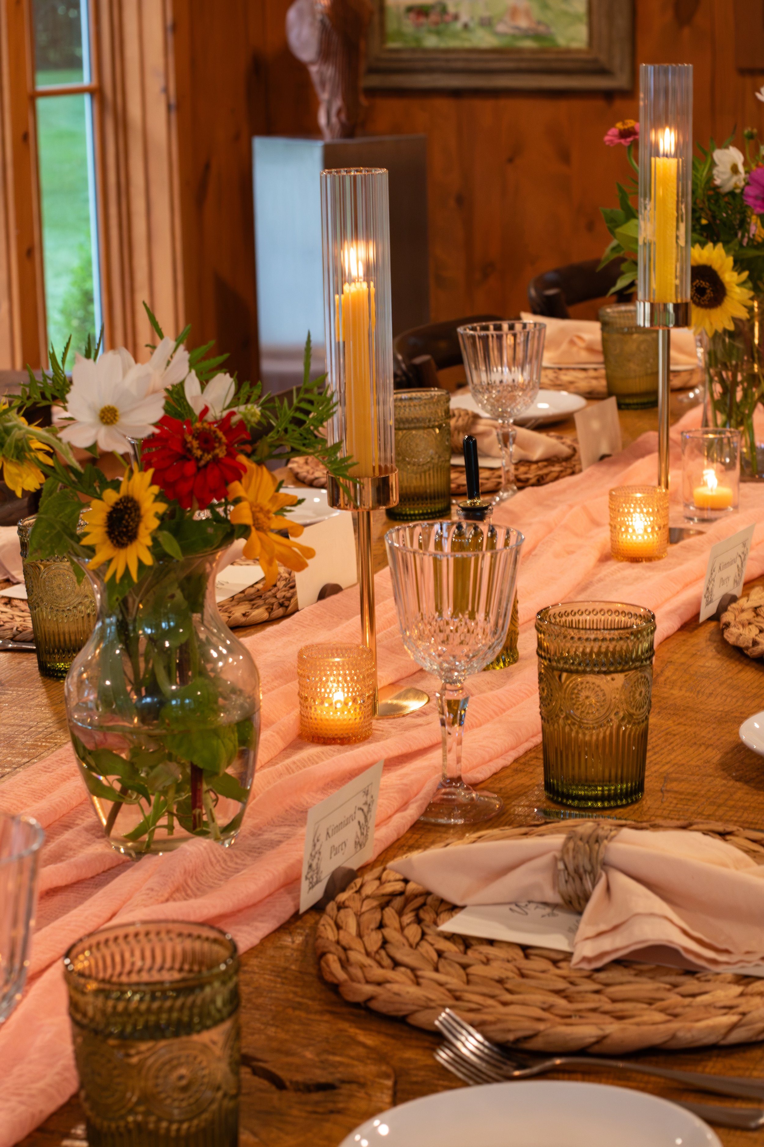 Decorated dining table with floral arrangements, candles, glassware, and table settings in a rustic wooden room.