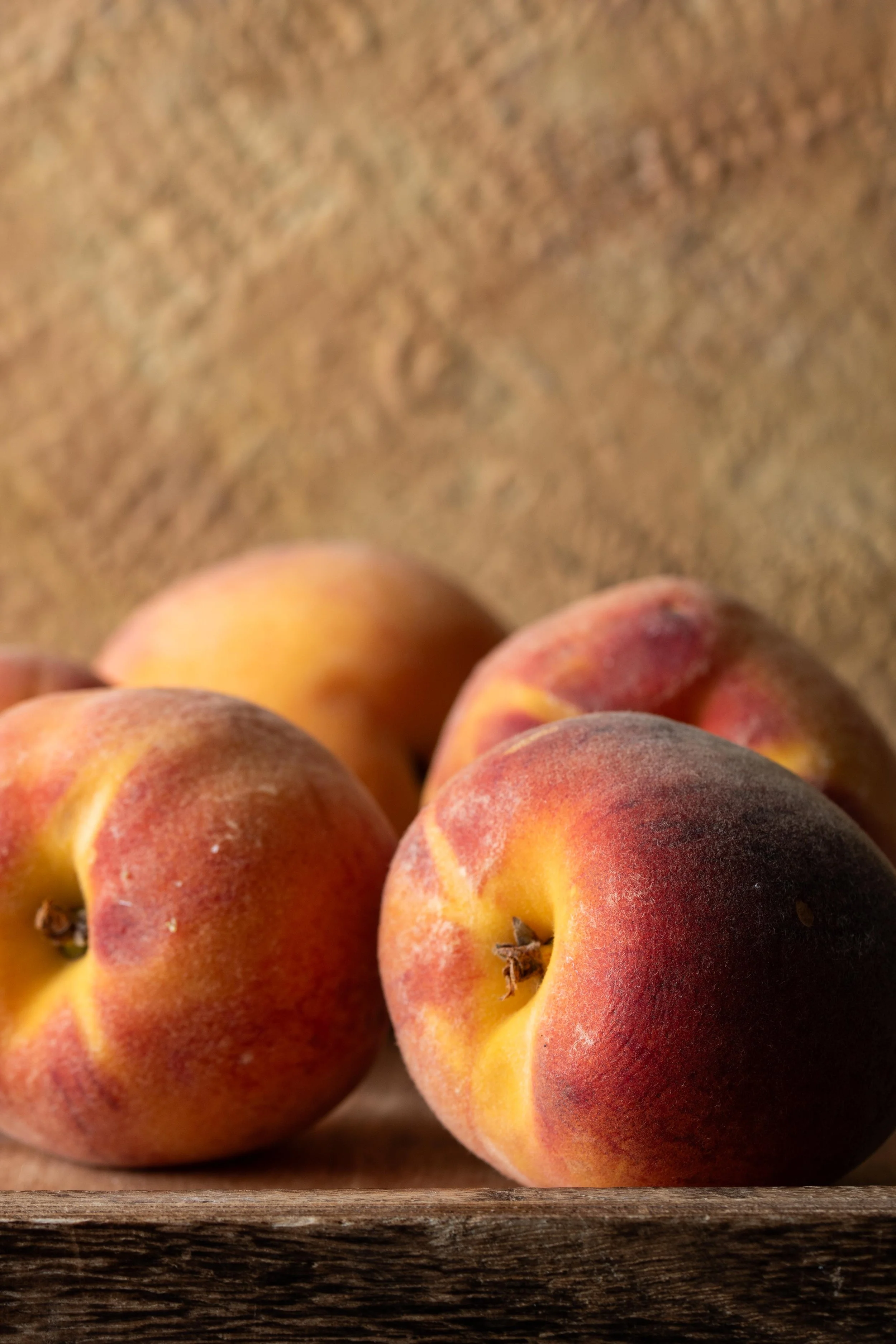 Close-up of peaches with fuzzy skin, resting on a wooden surface.
