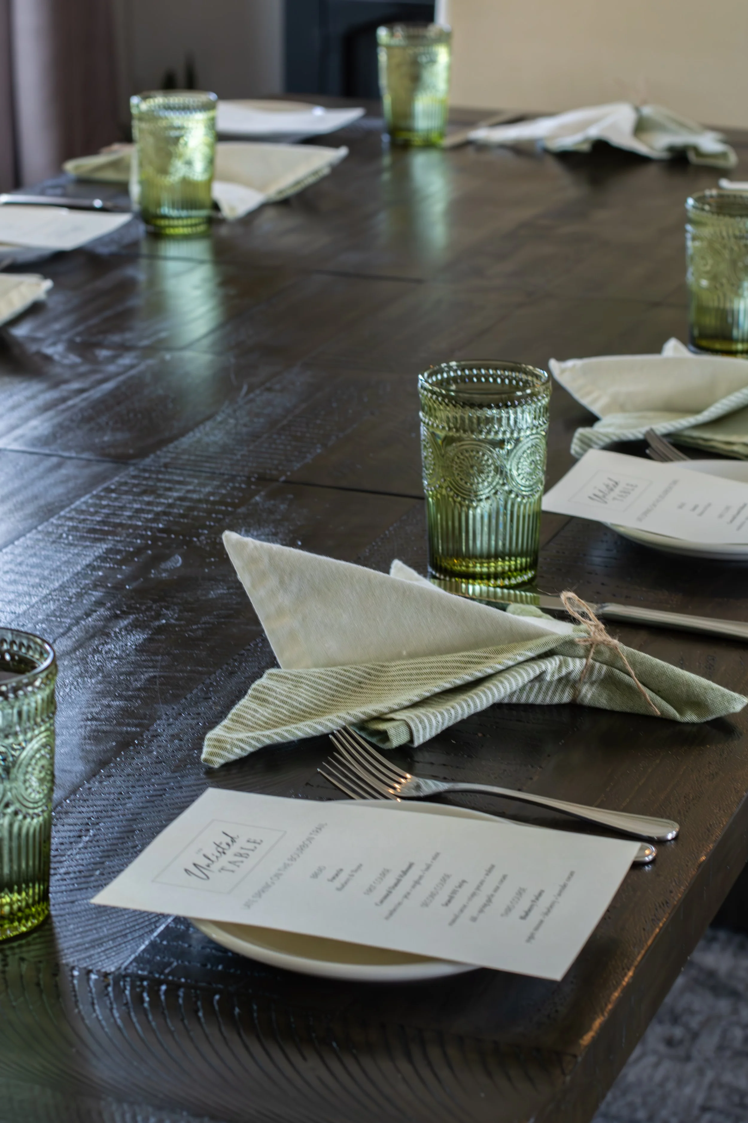 A dining table set with green glassware, white napkins, utensils, and printed menus.