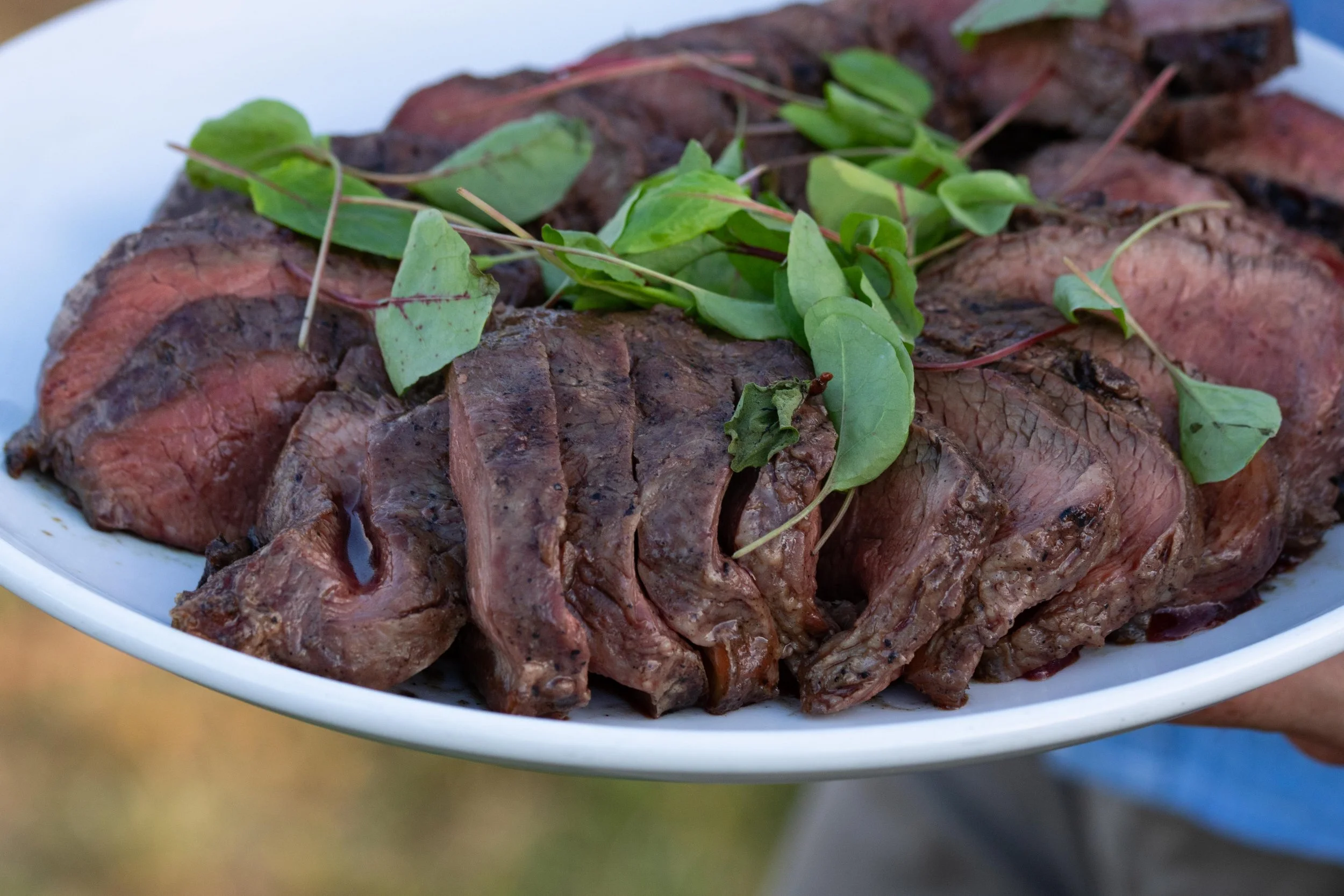 Plate of sliced cooked beef topped with fresh green herbs.