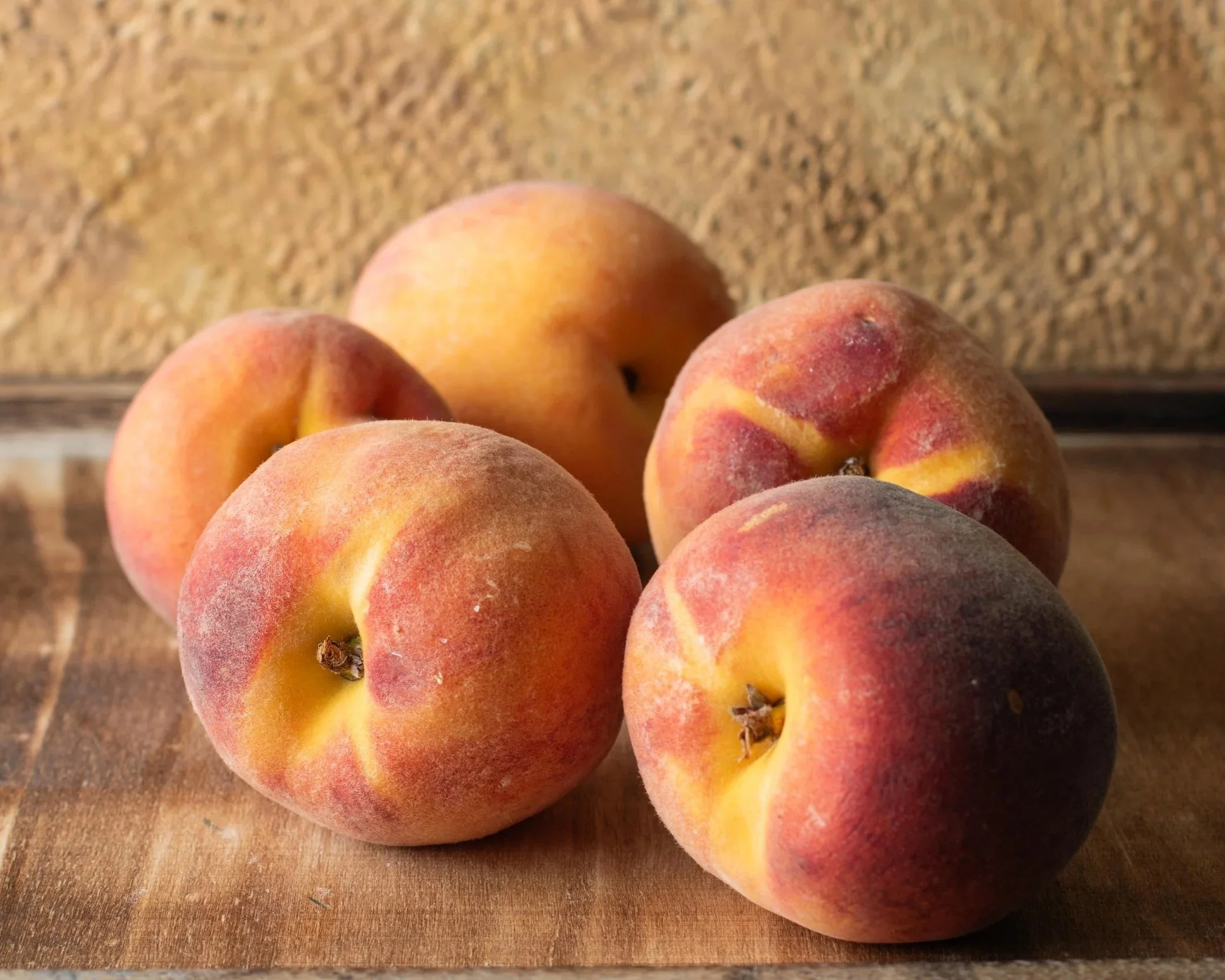 Close-up of several ripe peaches with fuzzy skin on a wooden surface.