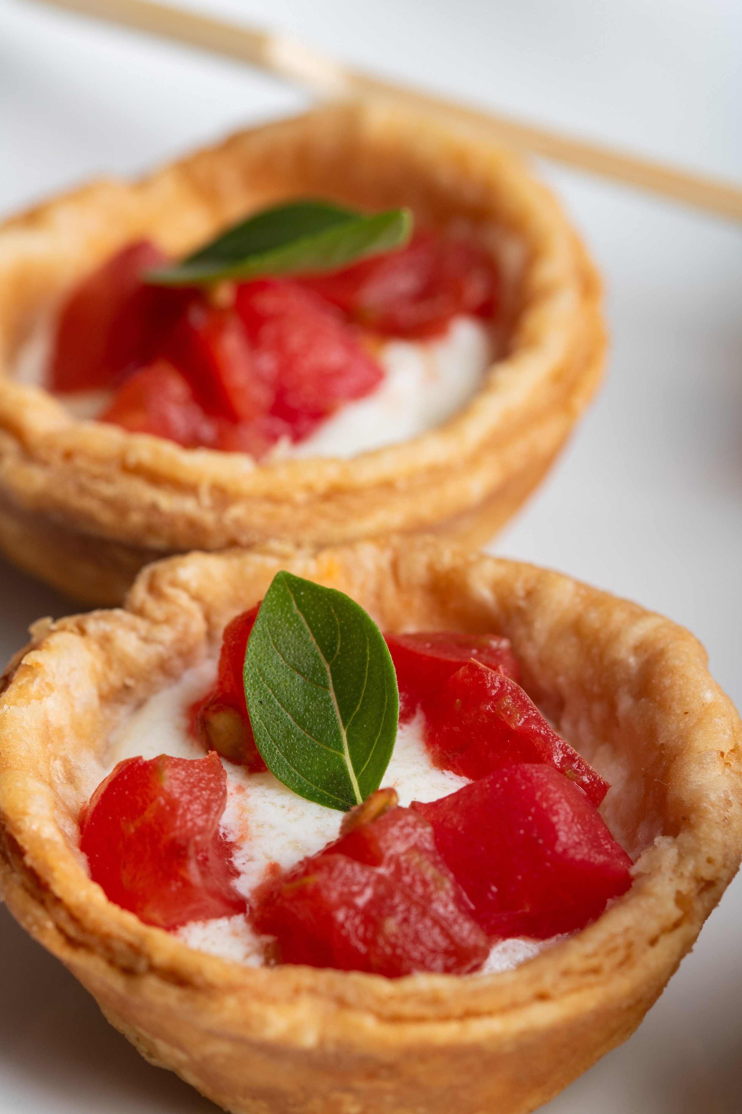 Close-up of a tart filled with cream, topped with strawberries and a green leaf, served on a white plate.
