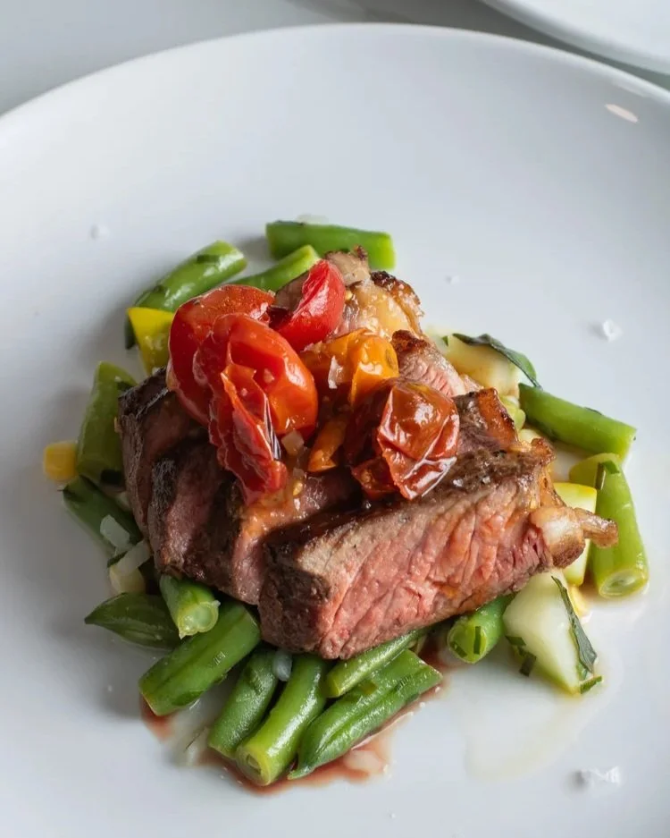 Grilled steak topped with cherry tomatoes and served on a bed of green beans and vegetables.