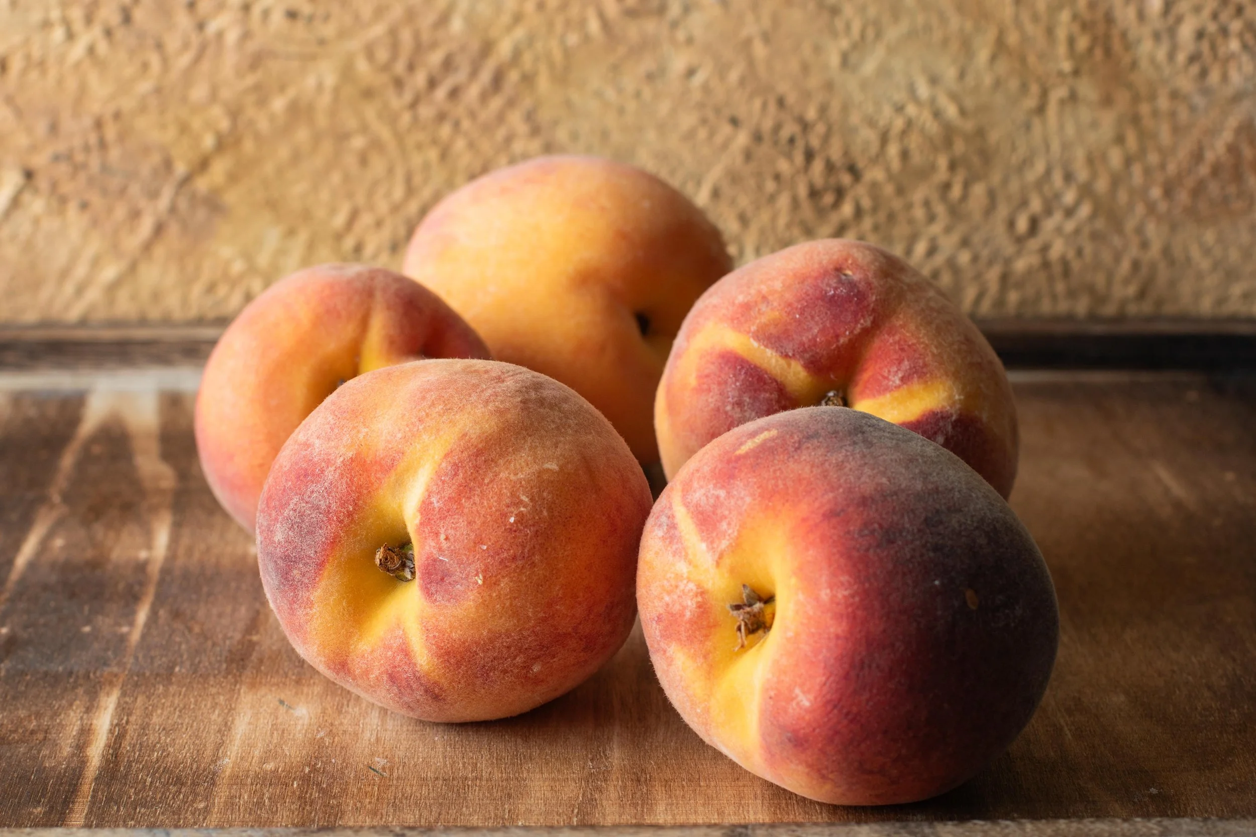 Five peaches on a wooden surface with a textured, brown background.