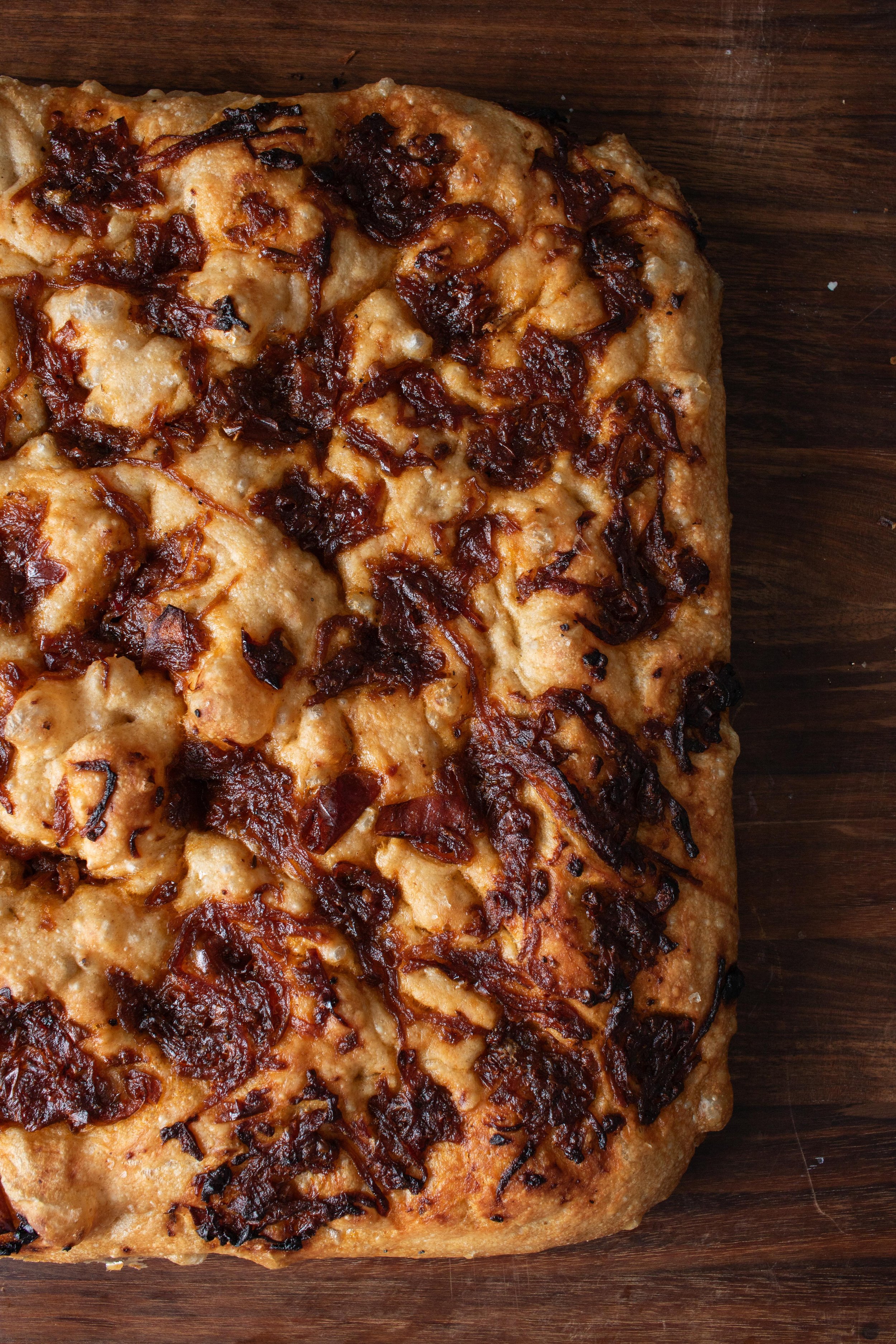 Close-up of a crispy, golden brown bacon and onion-topped homemade pizza on a wooden surface.