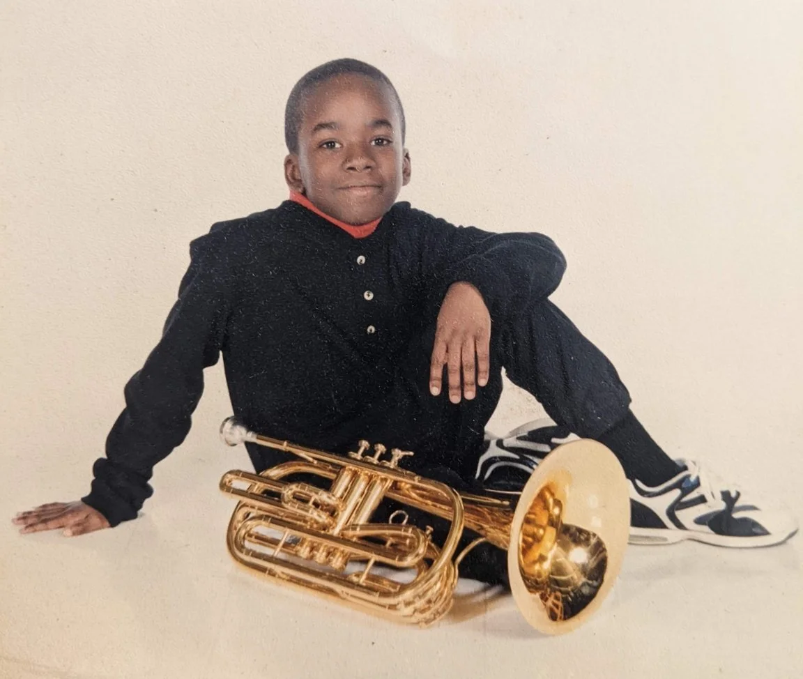 A young boy sitting on the floor with a gold-colored trumpet.
