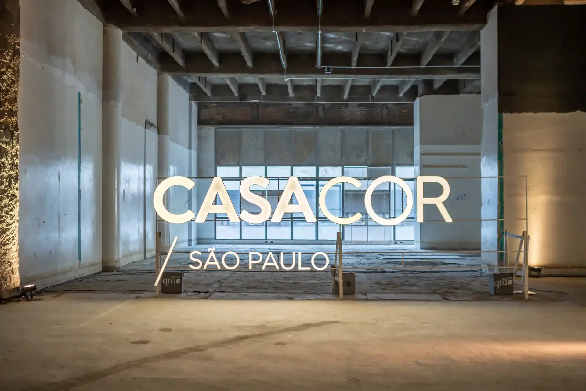 Leitão iluminado com o texto 'CASA COR SÃO PAULO' na frente, em ambiente de construção ou reforma.