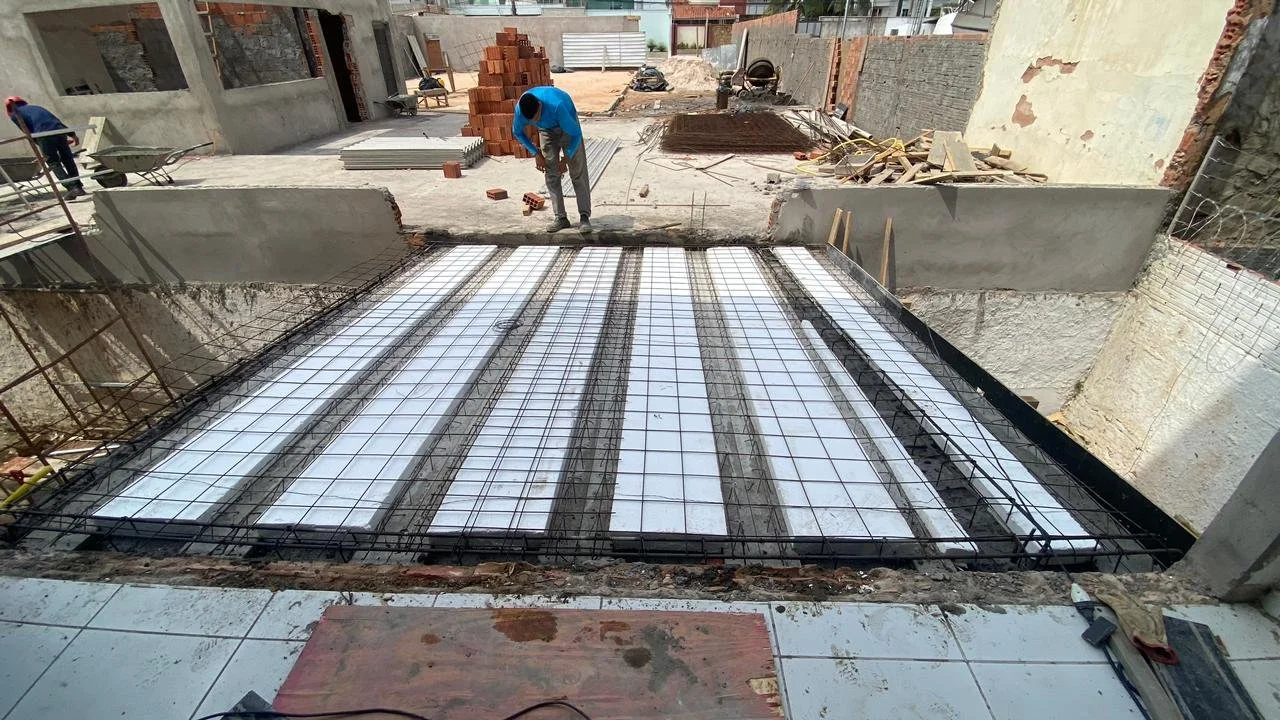 Construção de uma laje com reforço de aço e isolamento. Trabalho de obra com trabalhadores e materiais de construção ao fundo.
