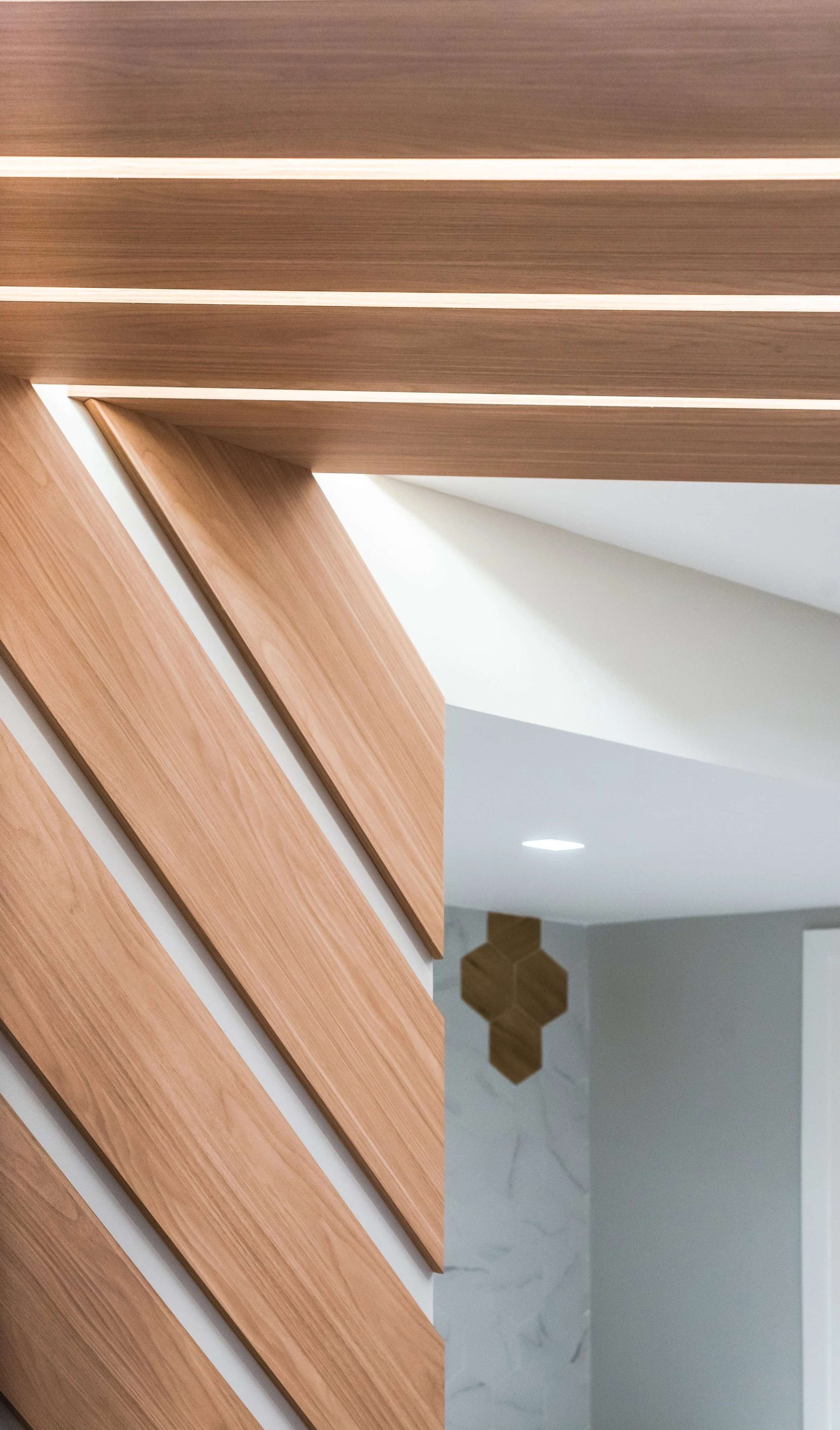 Detalhes de uma escultura de madeira com linhas diagonais e uma parede branca ao fundo, parte de um interior moderno.