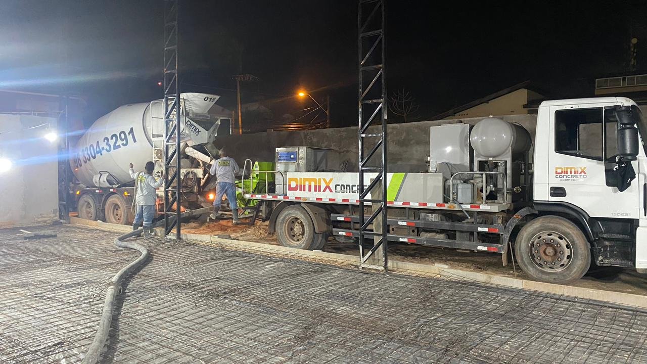 Caminhão betoneira em operação de concretagem na rua à noite, com três trabalhadores ao redor.